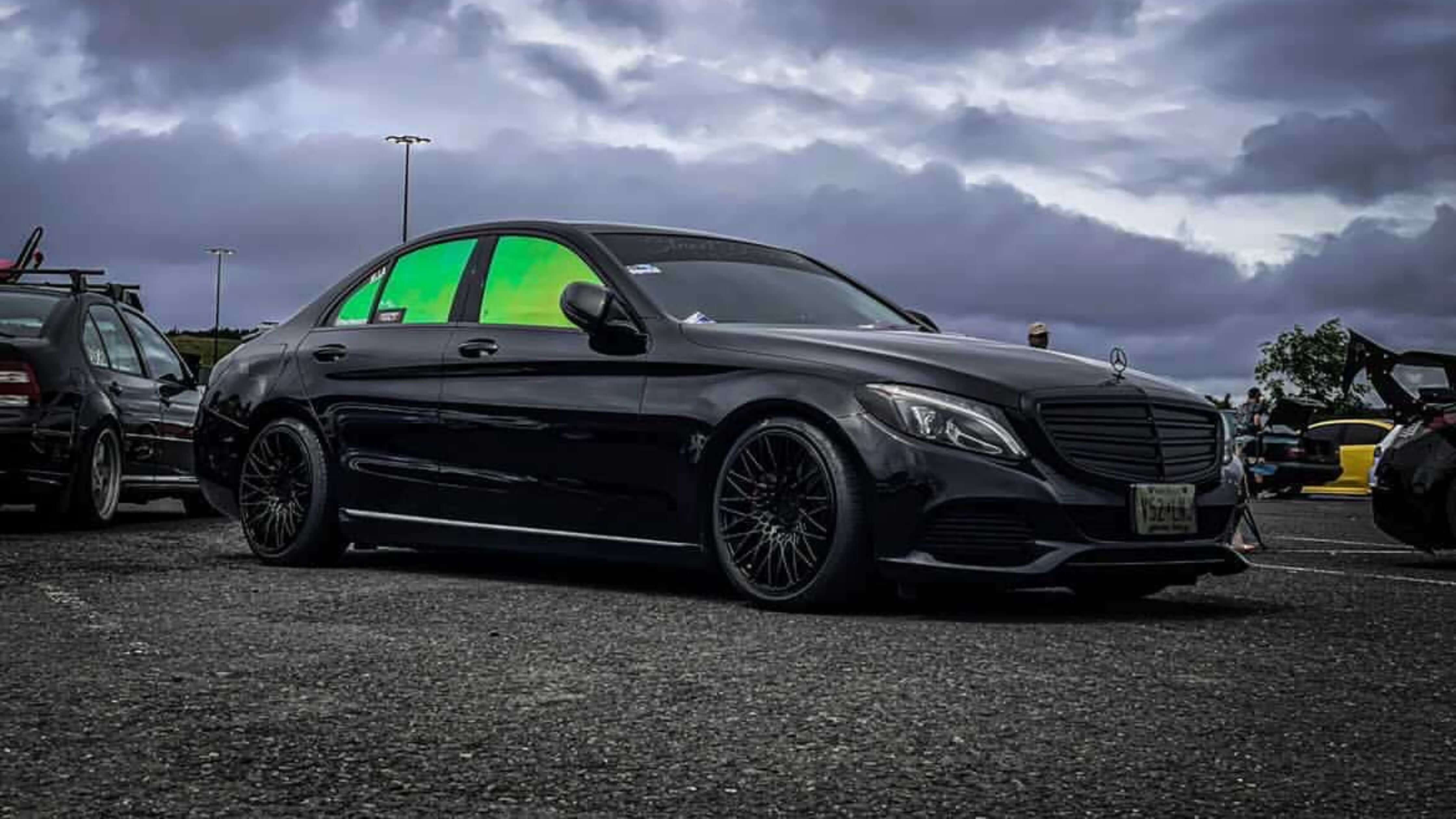 Sleek black car with tinted windows in a parking lot under a cloudy sky.