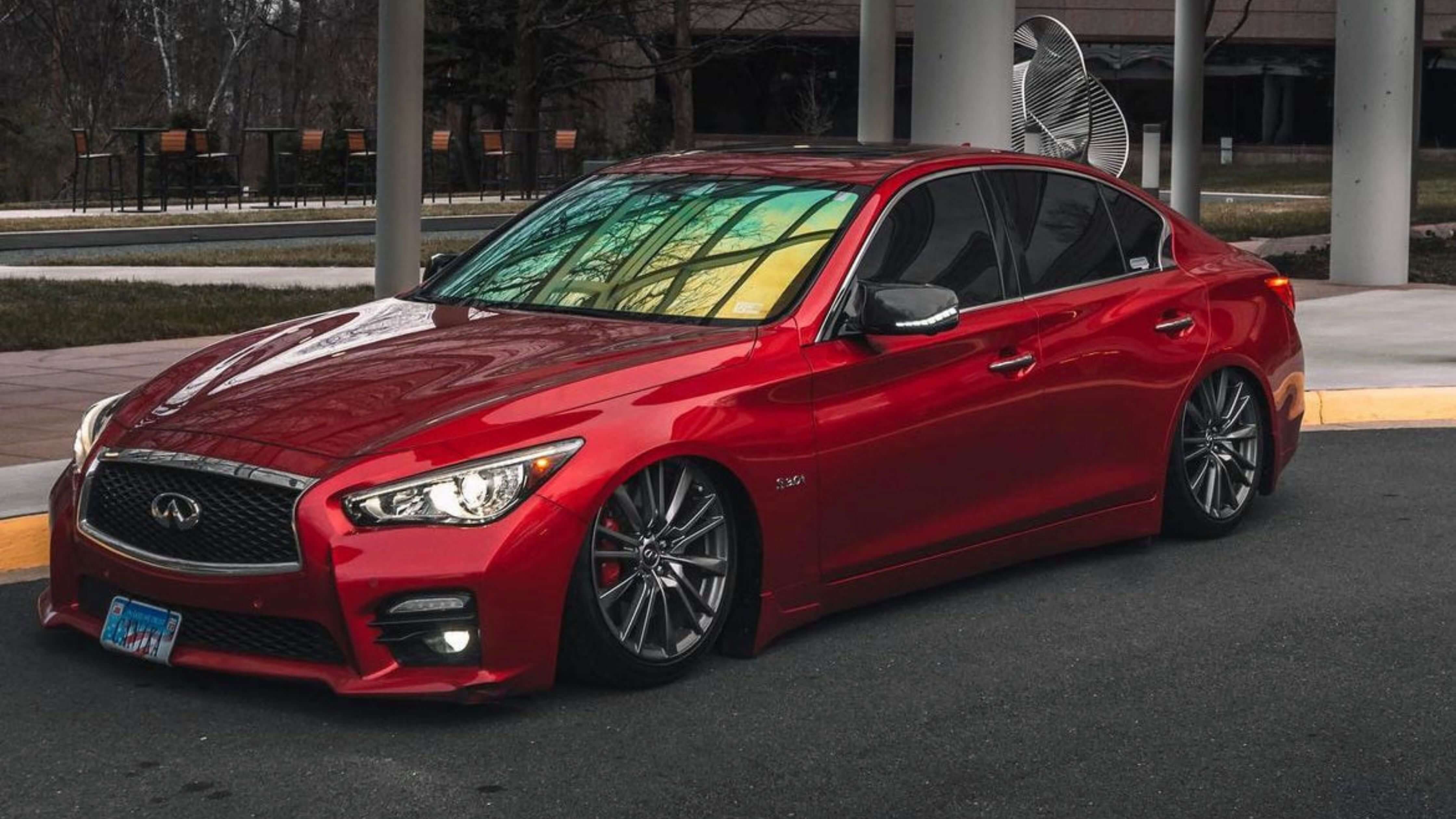 A red Infiniti sedan with tinted windows and custom wheels parked on a street, showcasing car window tinting results.