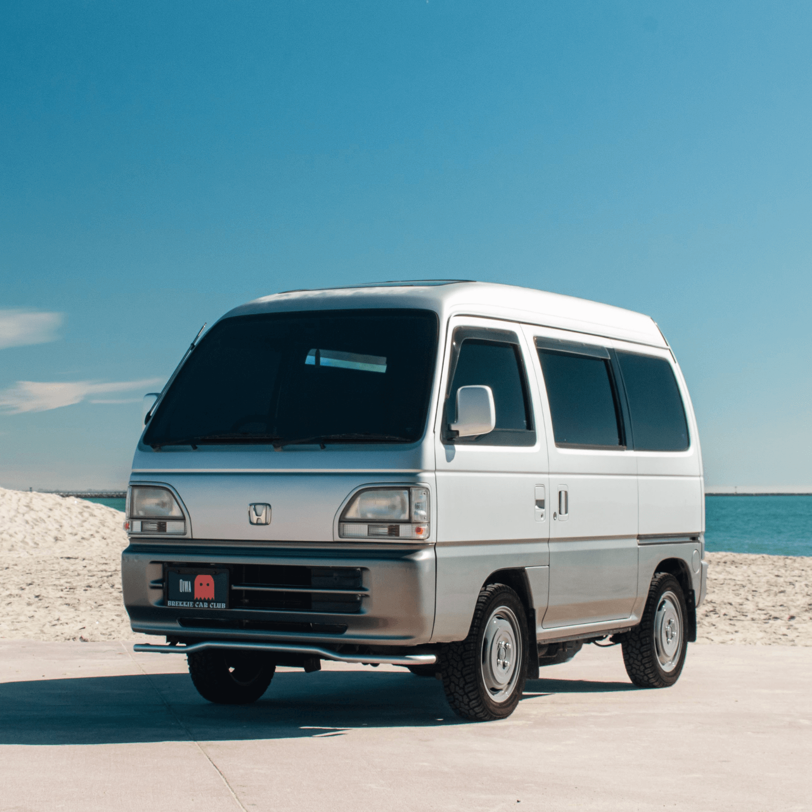 Honda Acty Van, a silver kei van featured in Oiwa Garage's comprehensive guide, parked on a sunny beach.