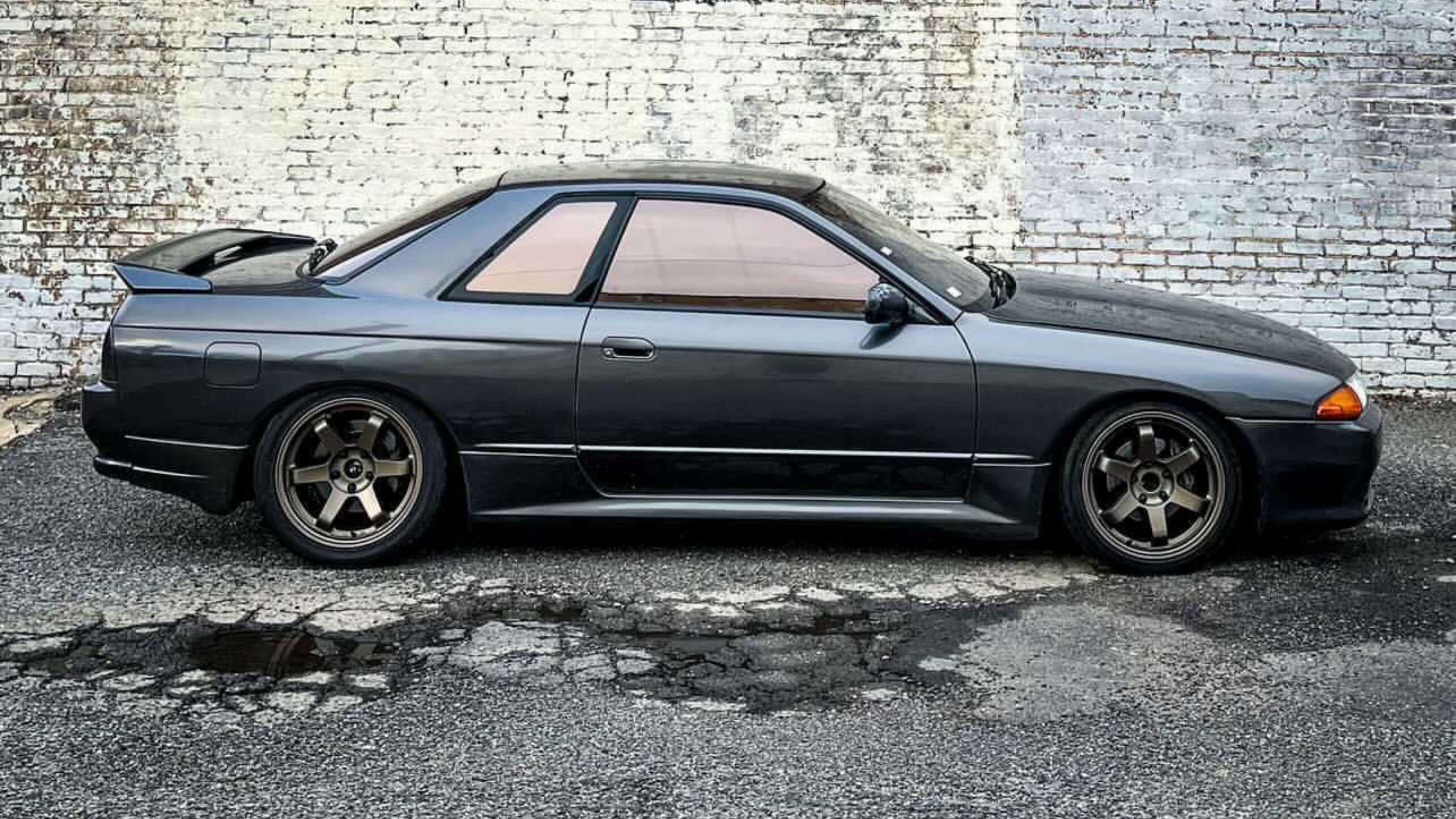 A sleek, dark gray sports car parked in front of a weathered white brick wall, perfect for DIY window tint removal.