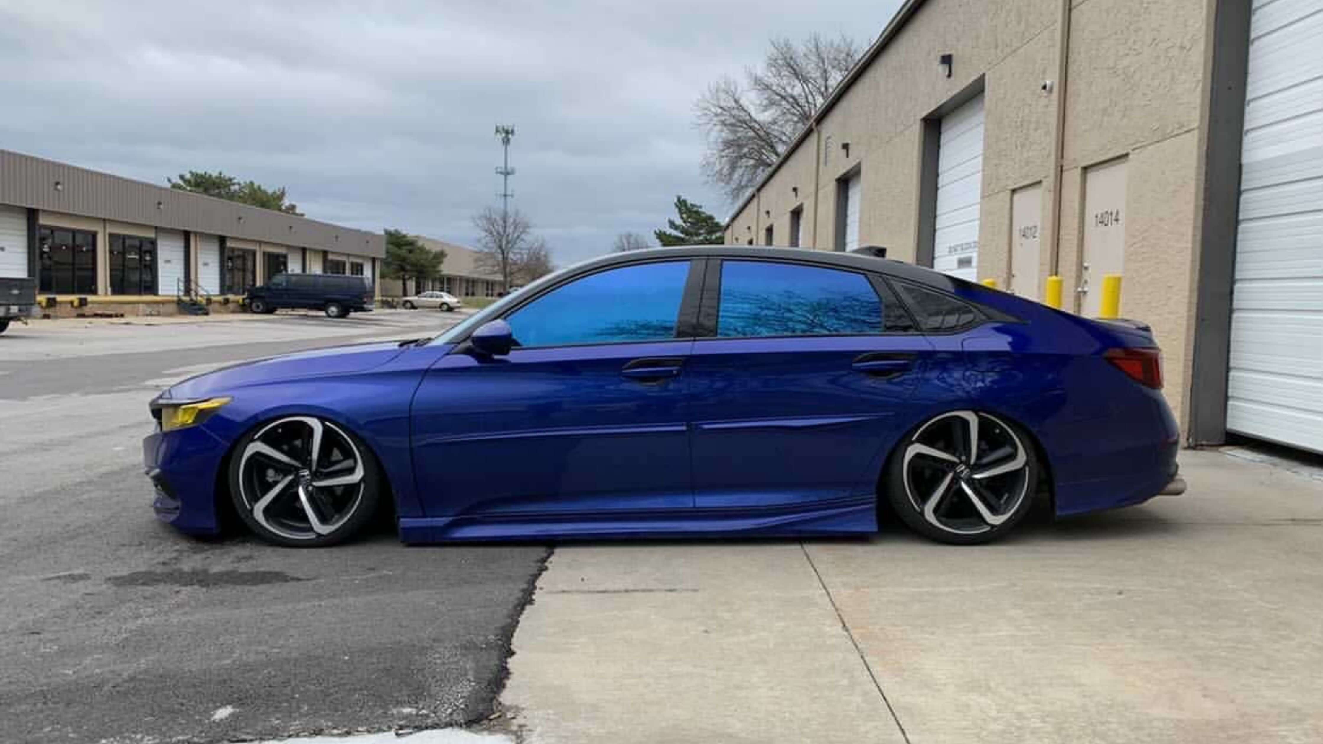 A blue sedan with tinted windows and custom wheels parked in an industrial area, showcasing stylish window tinting.