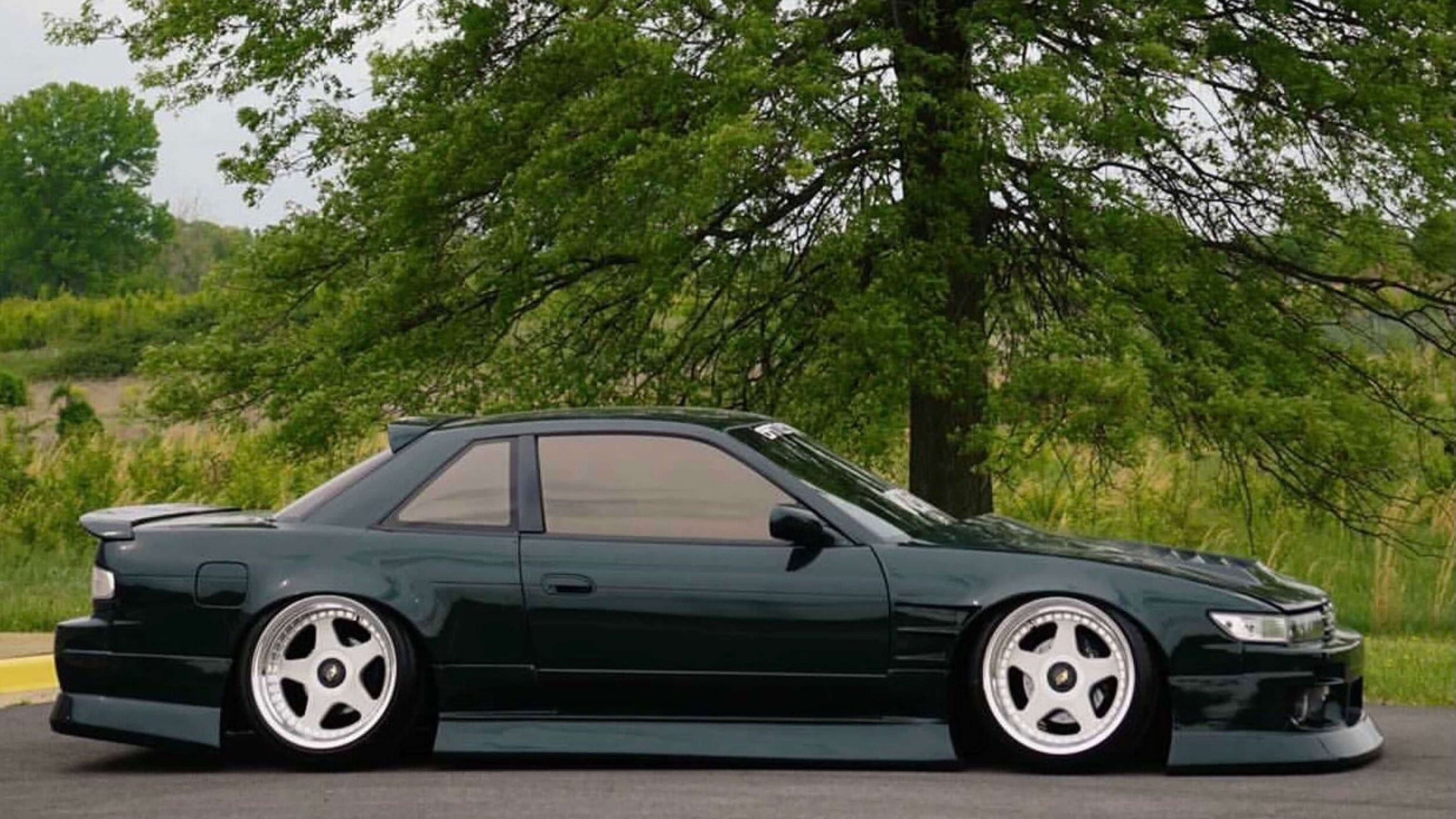 A dark green car with silver rims parked on a road, perfect for DIY tint removal.