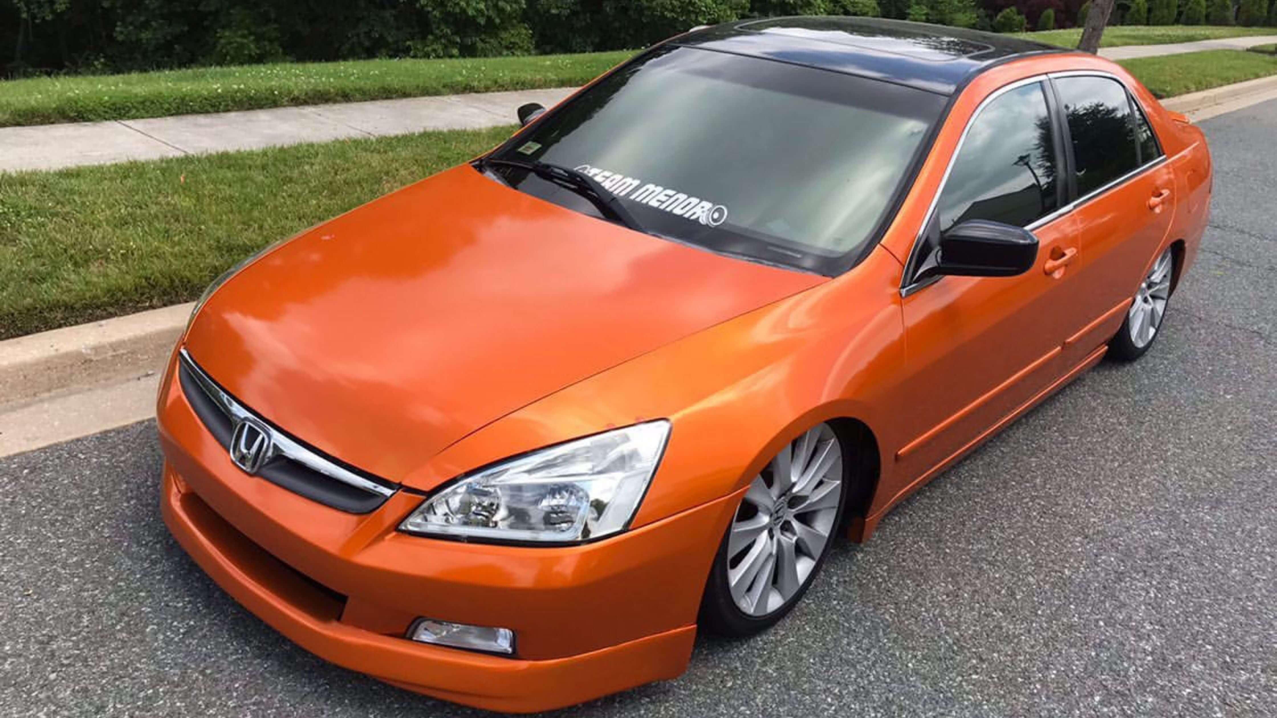 Bright orange Honda sedan with tinted windows parked on a sunny street.