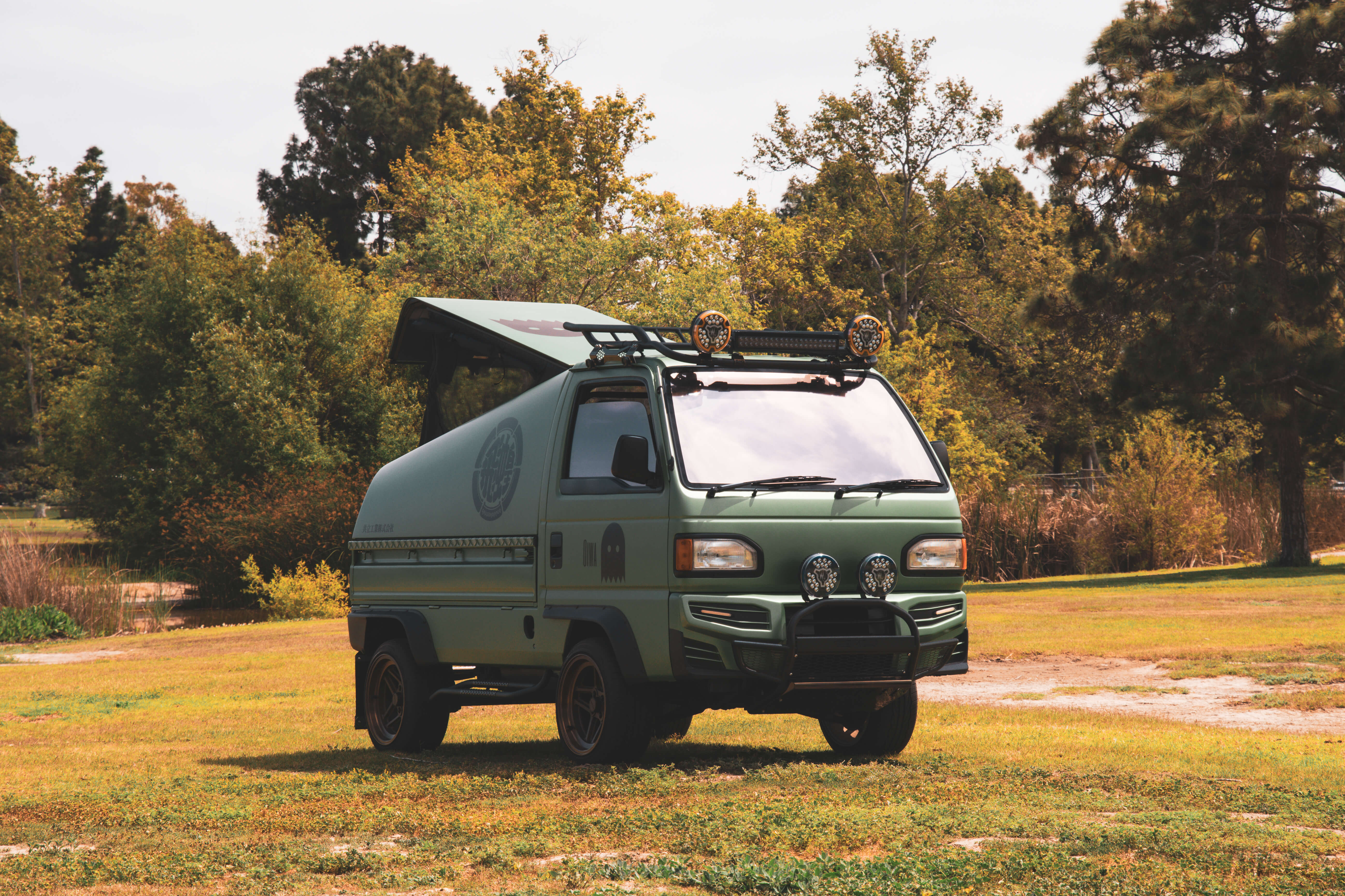 Grasshopper Honda Acty Camper parked outdoors, featuring lifted suspension, off-road wheels, custom camper shell, roof rack, and brush guard.
