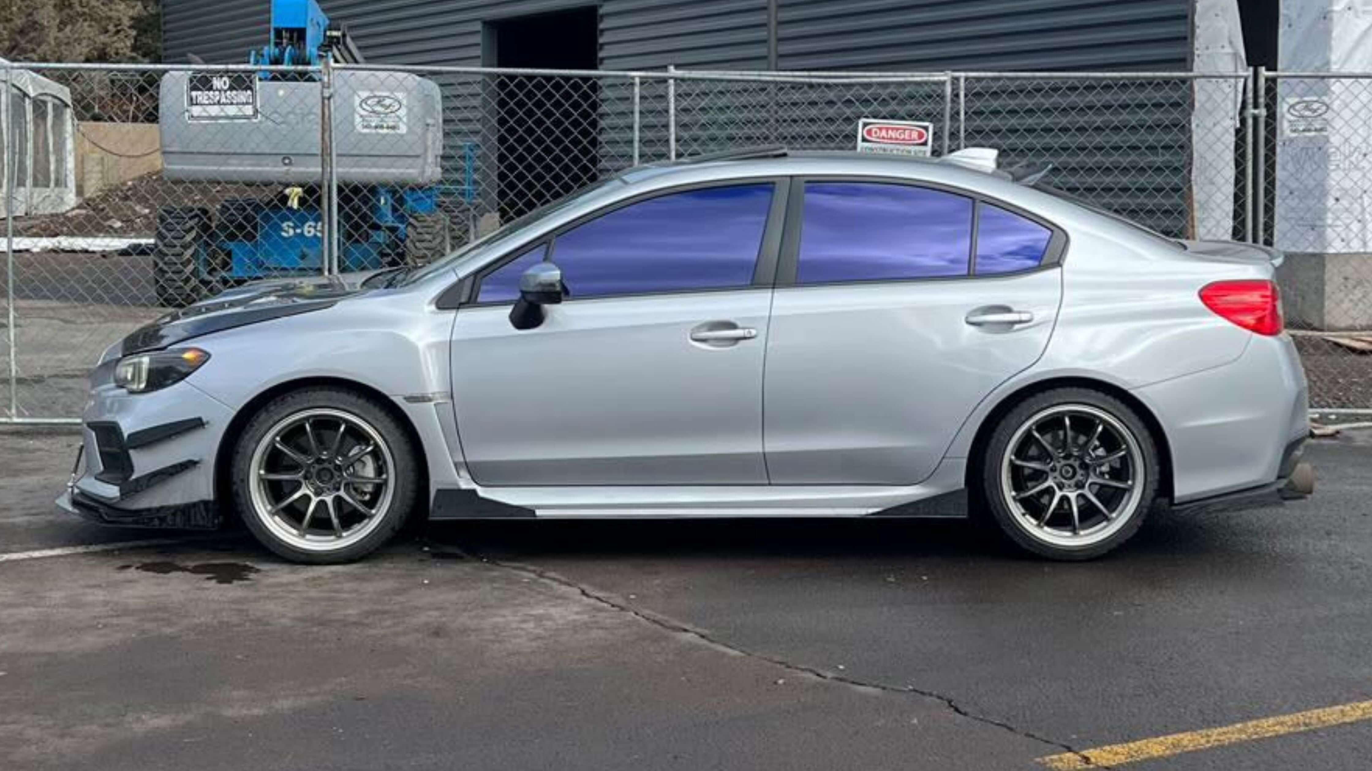 A silver sedan with tinted windows parked near construction equipment, showcasing the tinting process for a 4-door car.