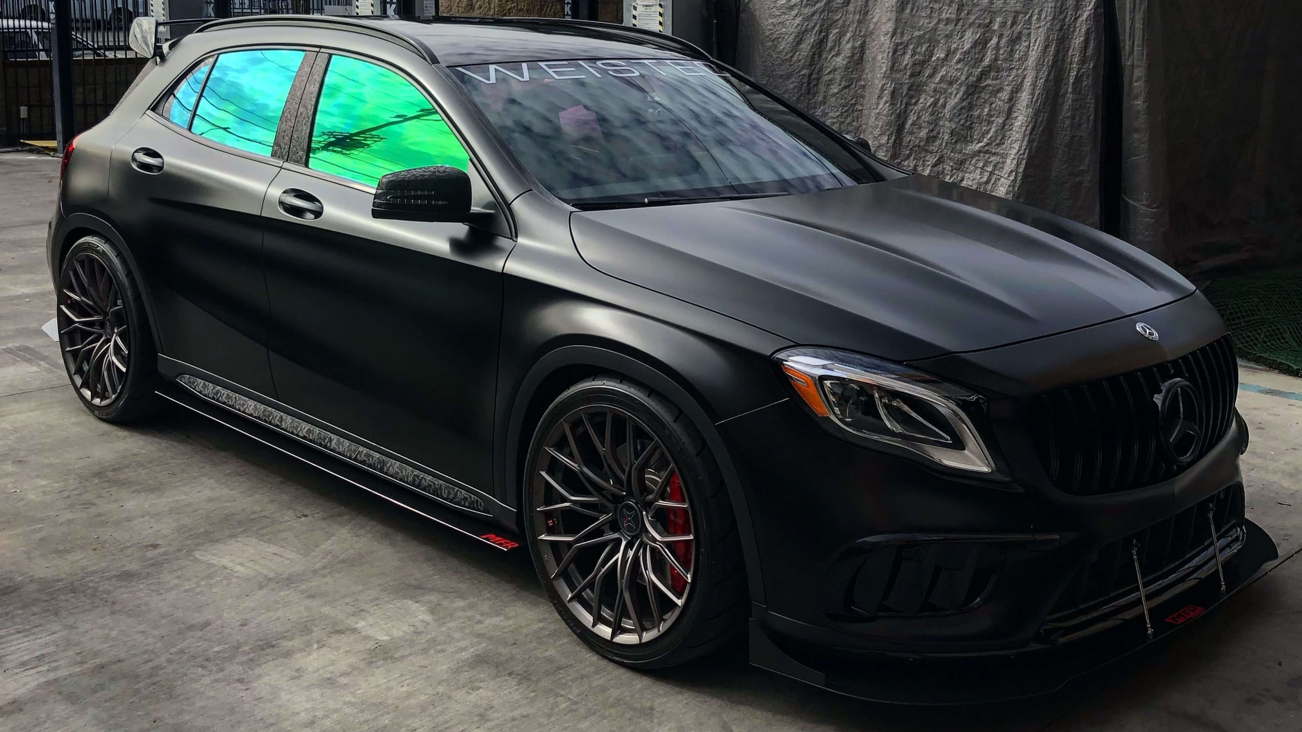A sleek, matte black Mercedes-Benz car with tinted windows and custom wheels parked in a garage, illustrating car tinting time.
