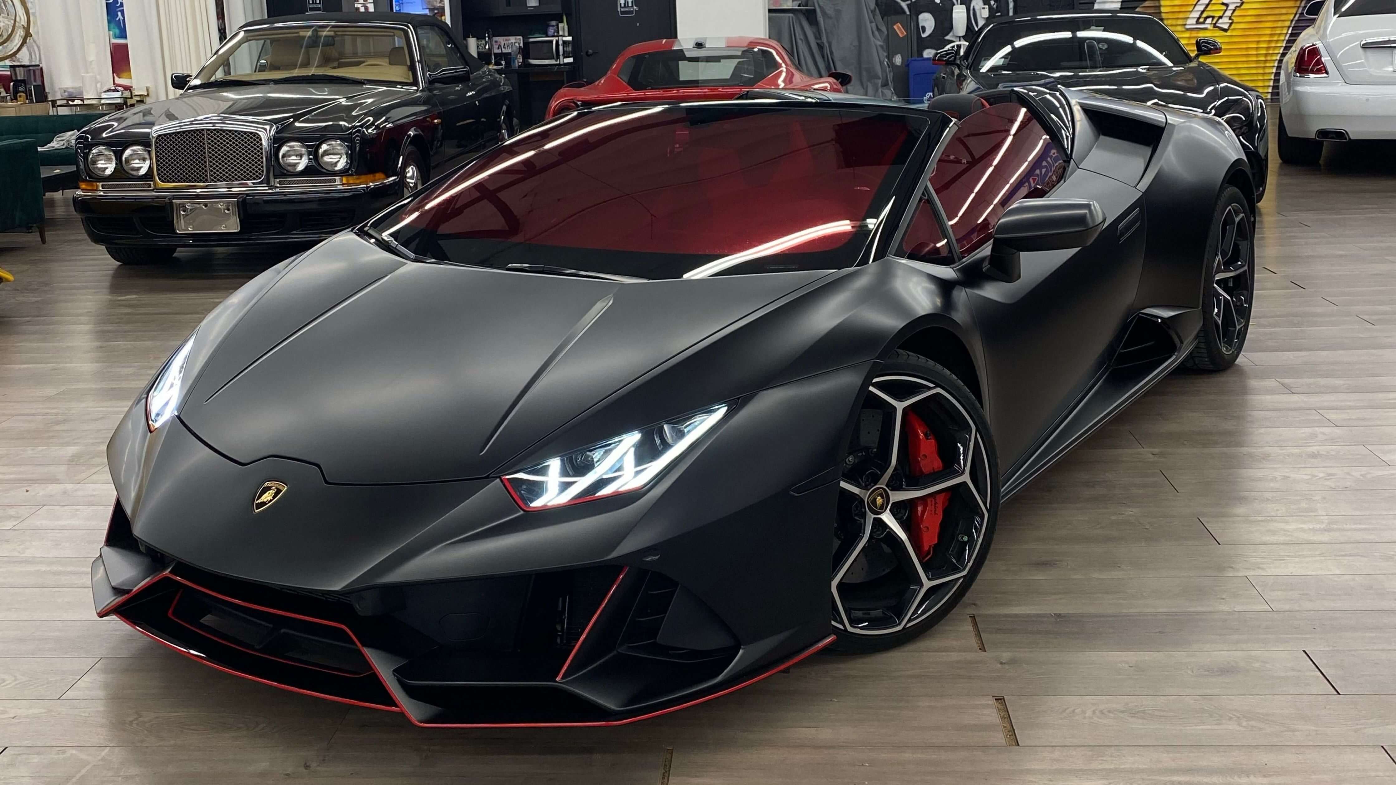 A sleek, matte black Lamborghini with tinted windows parked among luxury cars, showcasing the allure of window tinting.