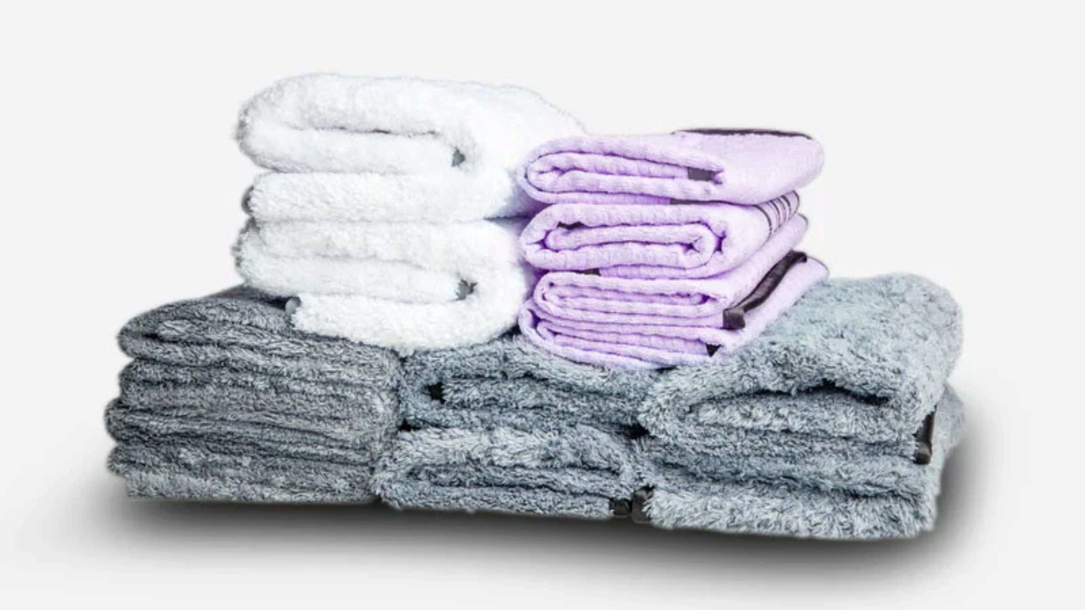 A stack of folded microfiber towels in white, lavender, and gray, ideal for cleaning glasses.