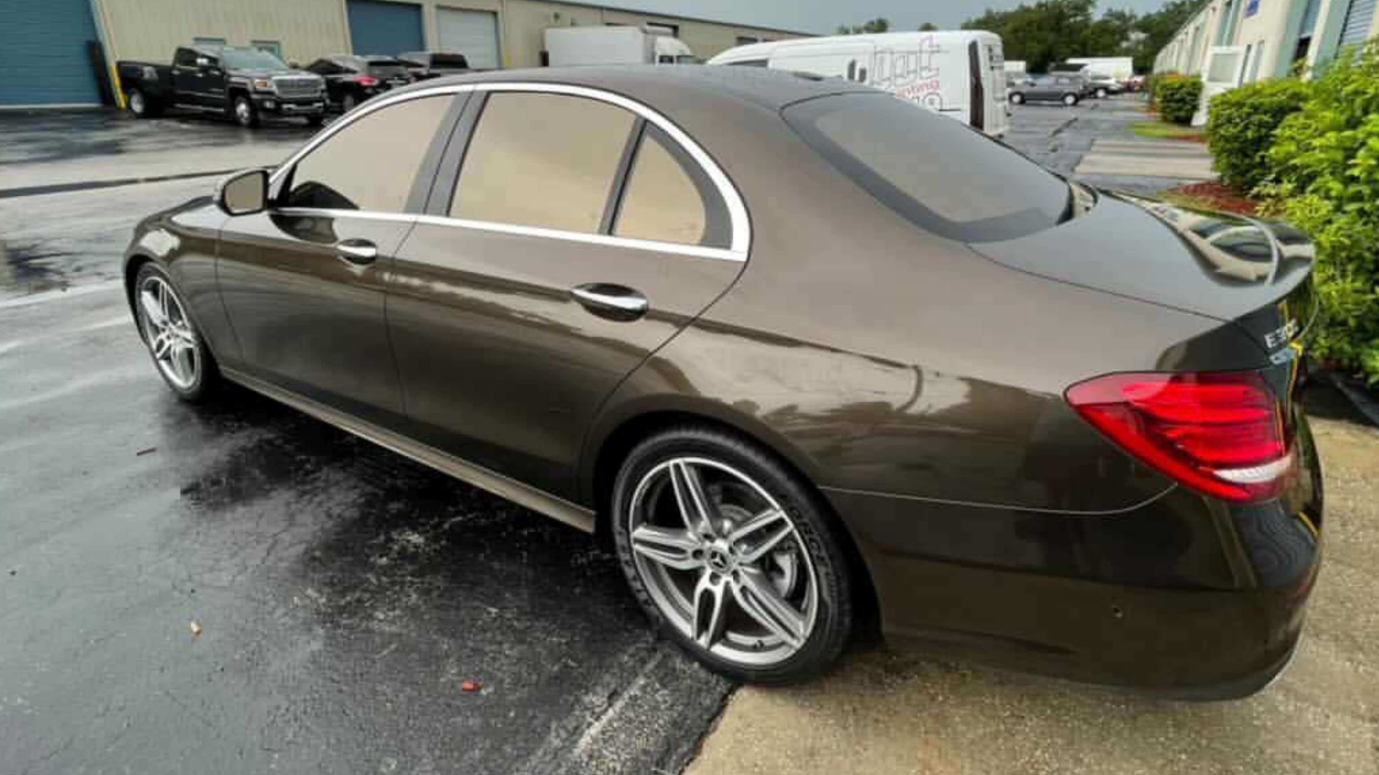 Brown luxury sedan on wet pavement, showcasing post-tint care.