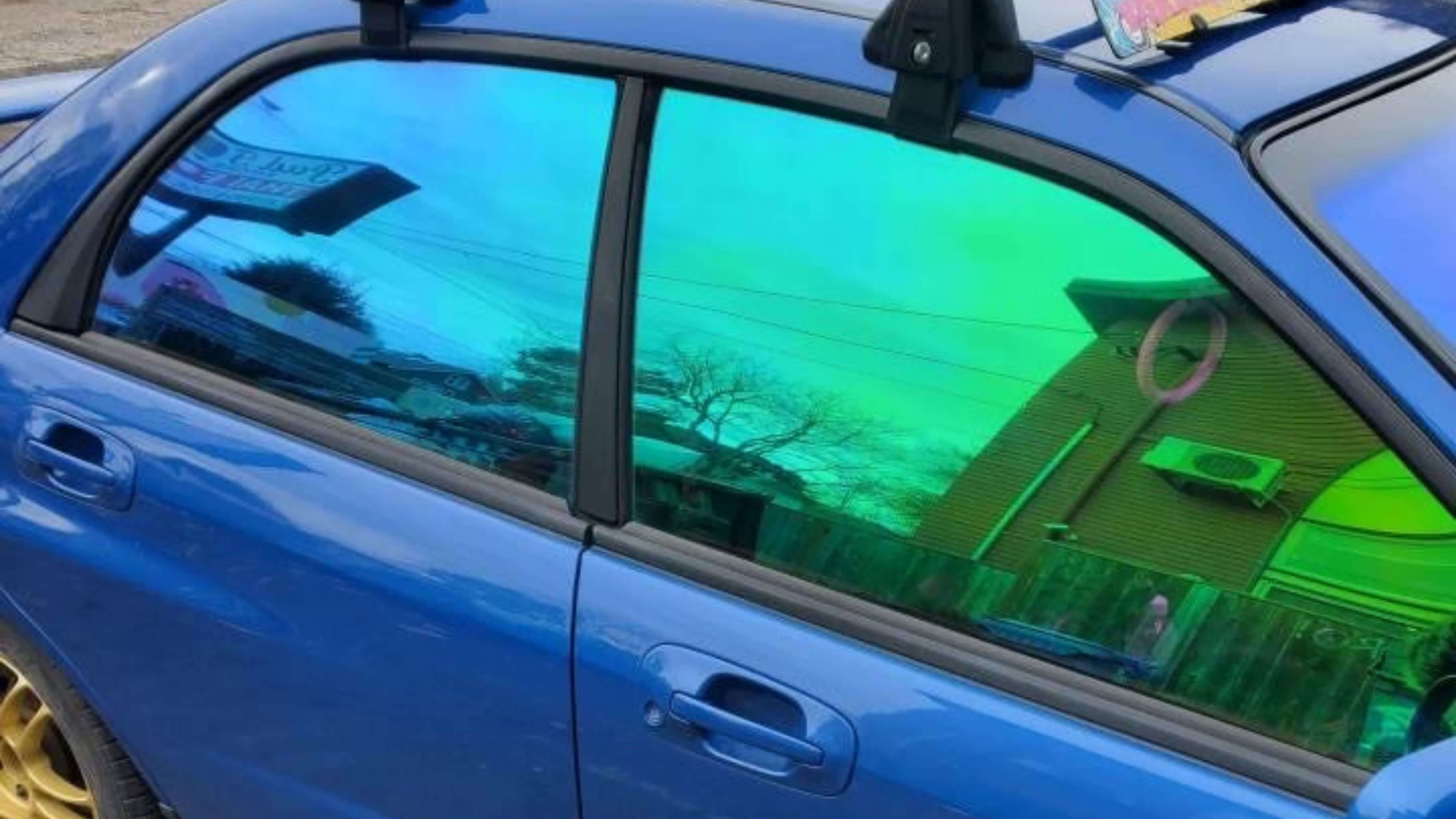 A blue car with green-tinted windows reflecting the surrounding environment.