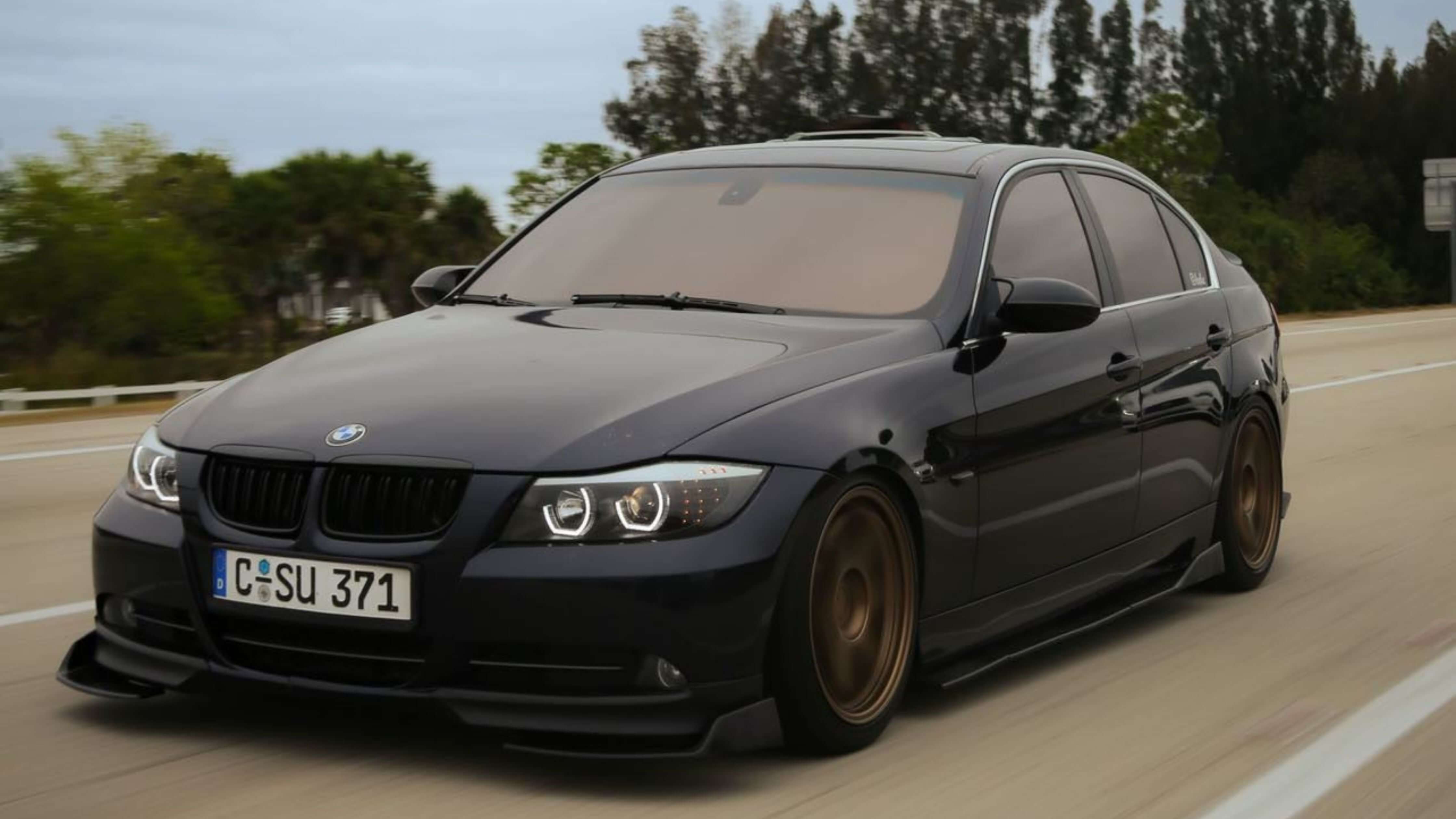 A black BMW sedan with tinted windows and custom wheels driving on a highway.