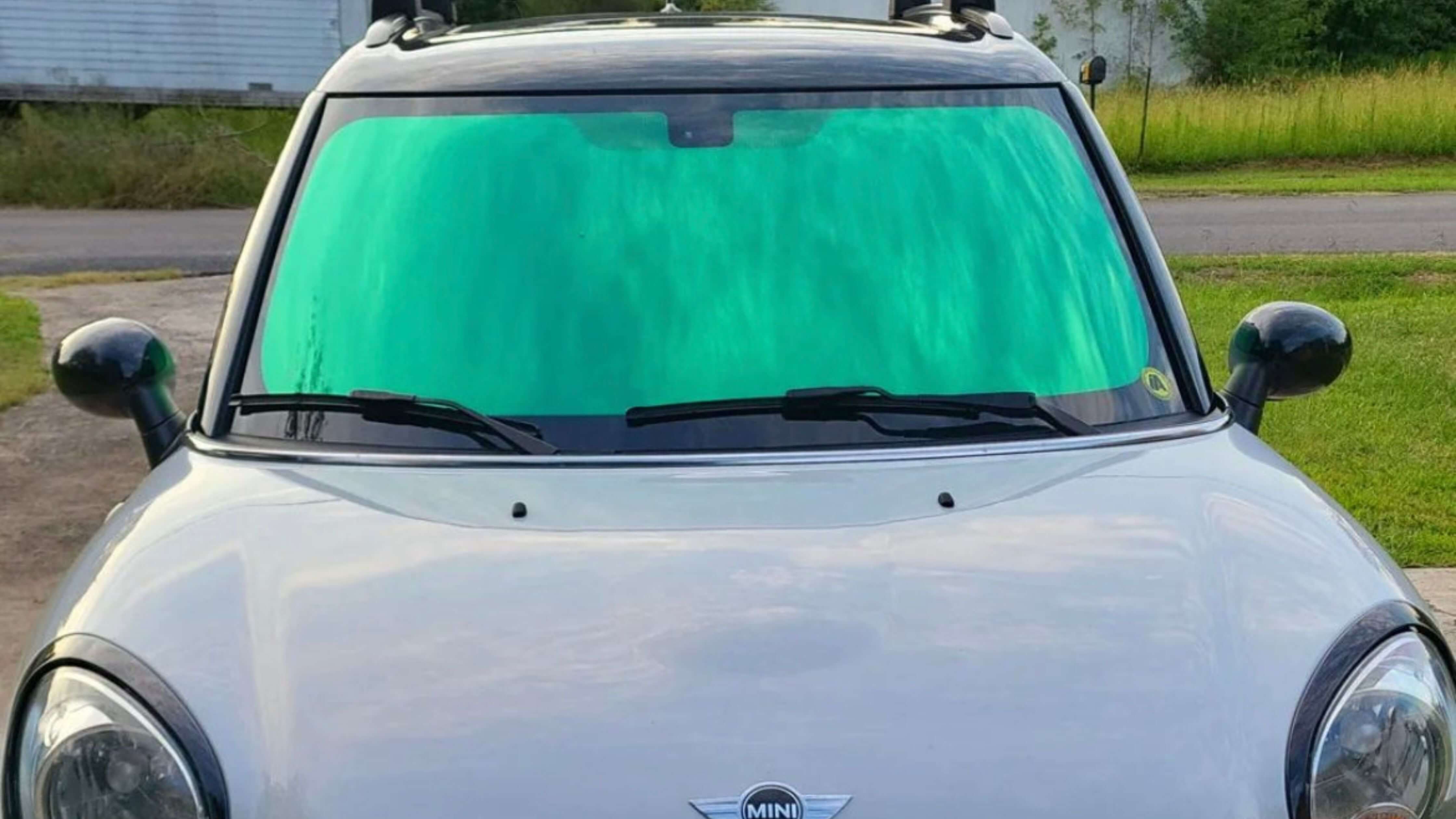 A white Mini Cooper with a bright green sunshade covering the windshield, parked outdoors.