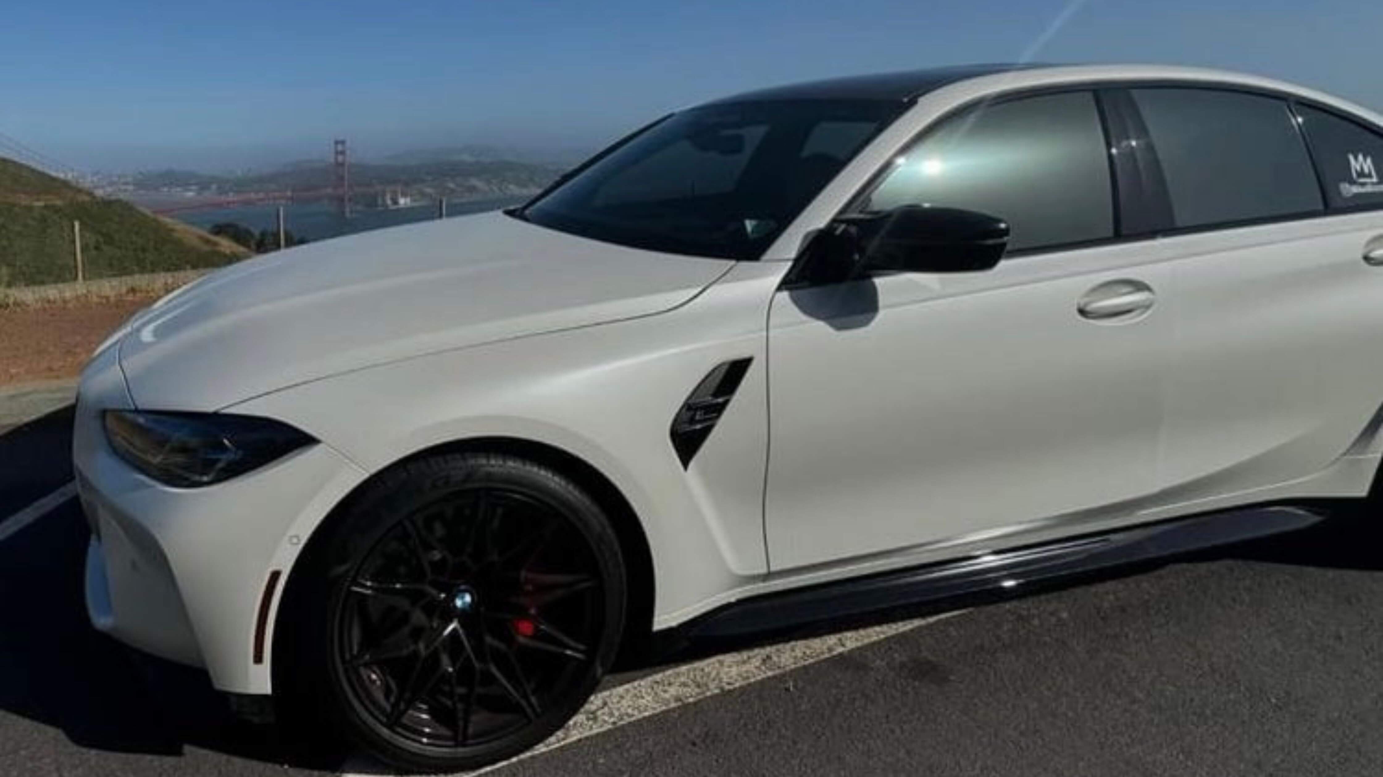 A white sports car with tinted windows, parked near the Golden Gate Bridge.