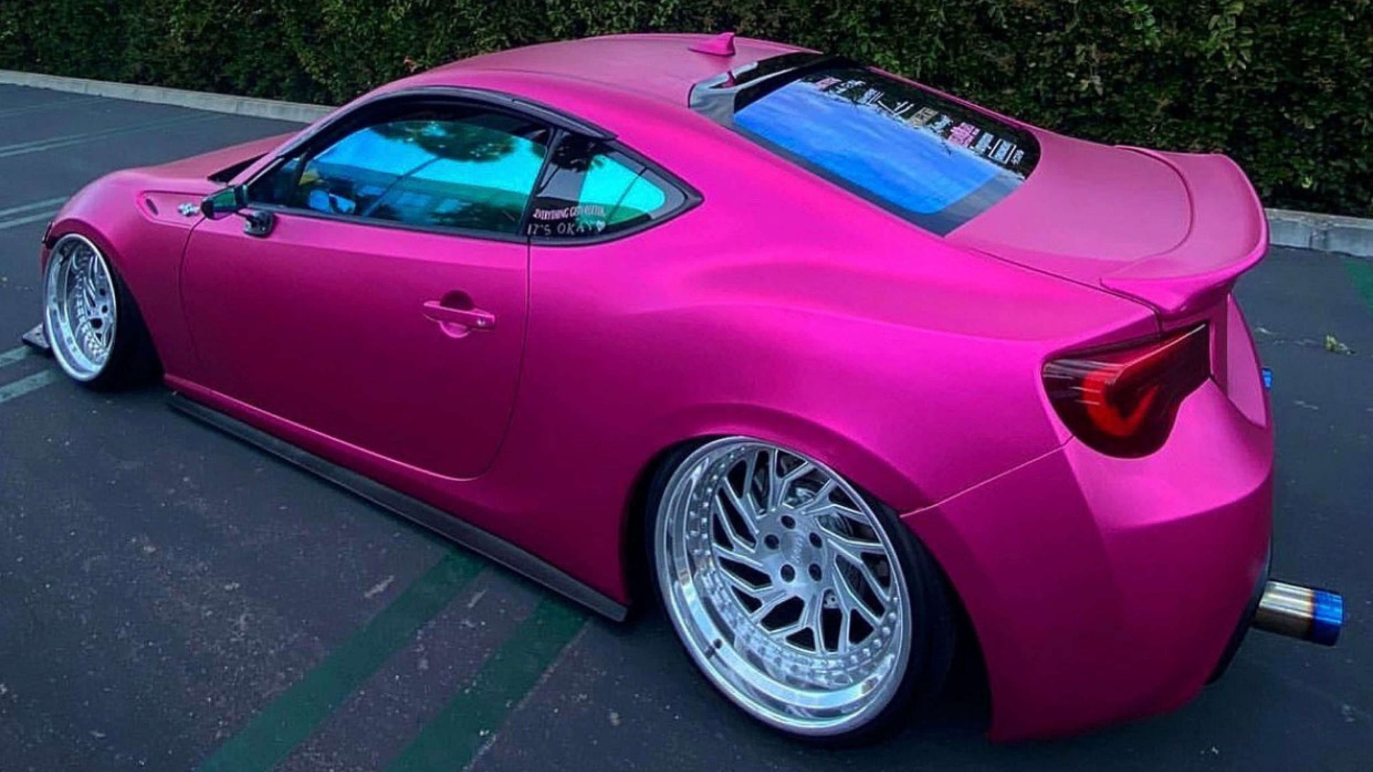 Professional car window tinting process on a bright pink sports car.
