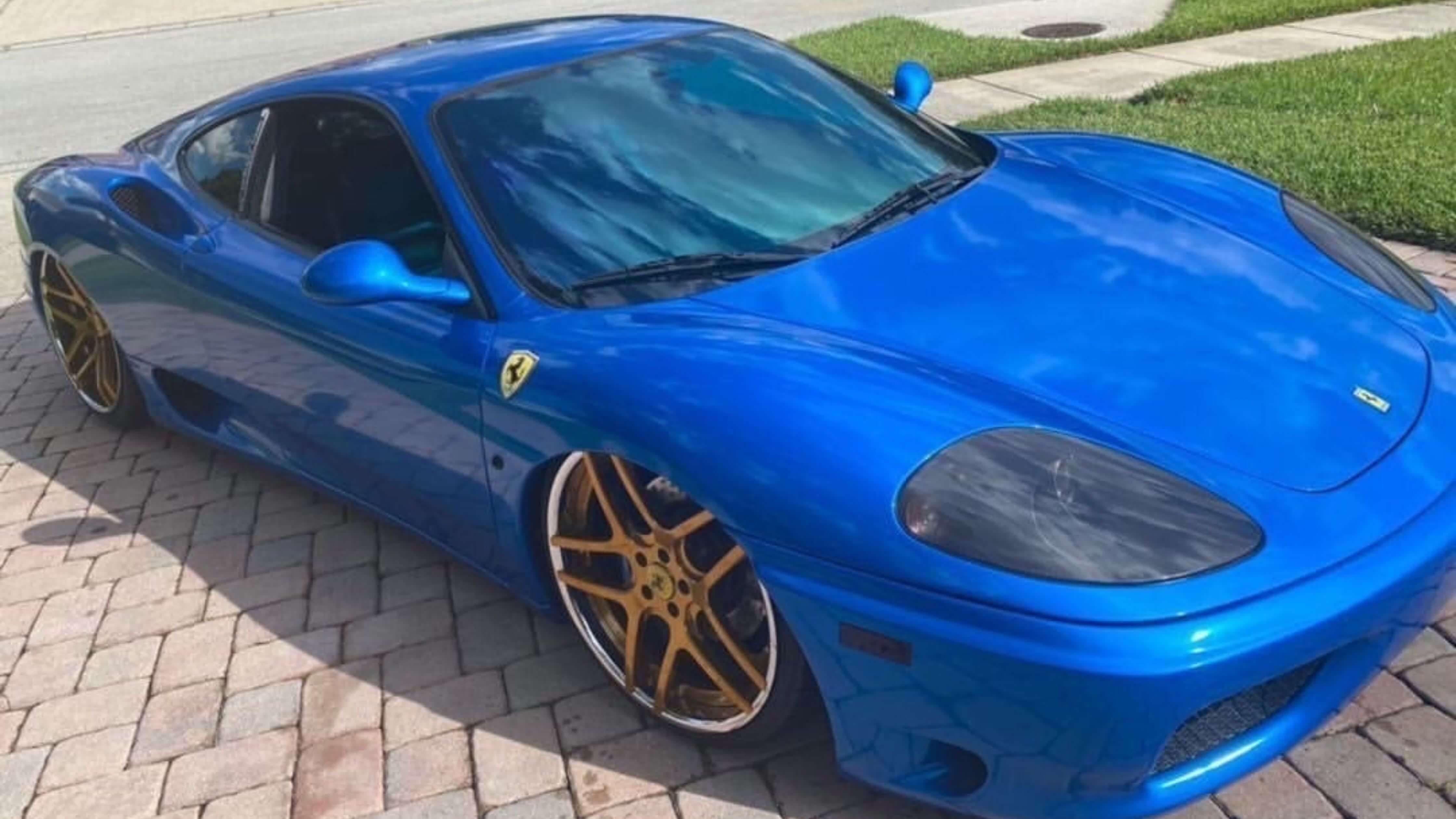 Blue sports car with gold rims on brick driveway, showcasing window tint.