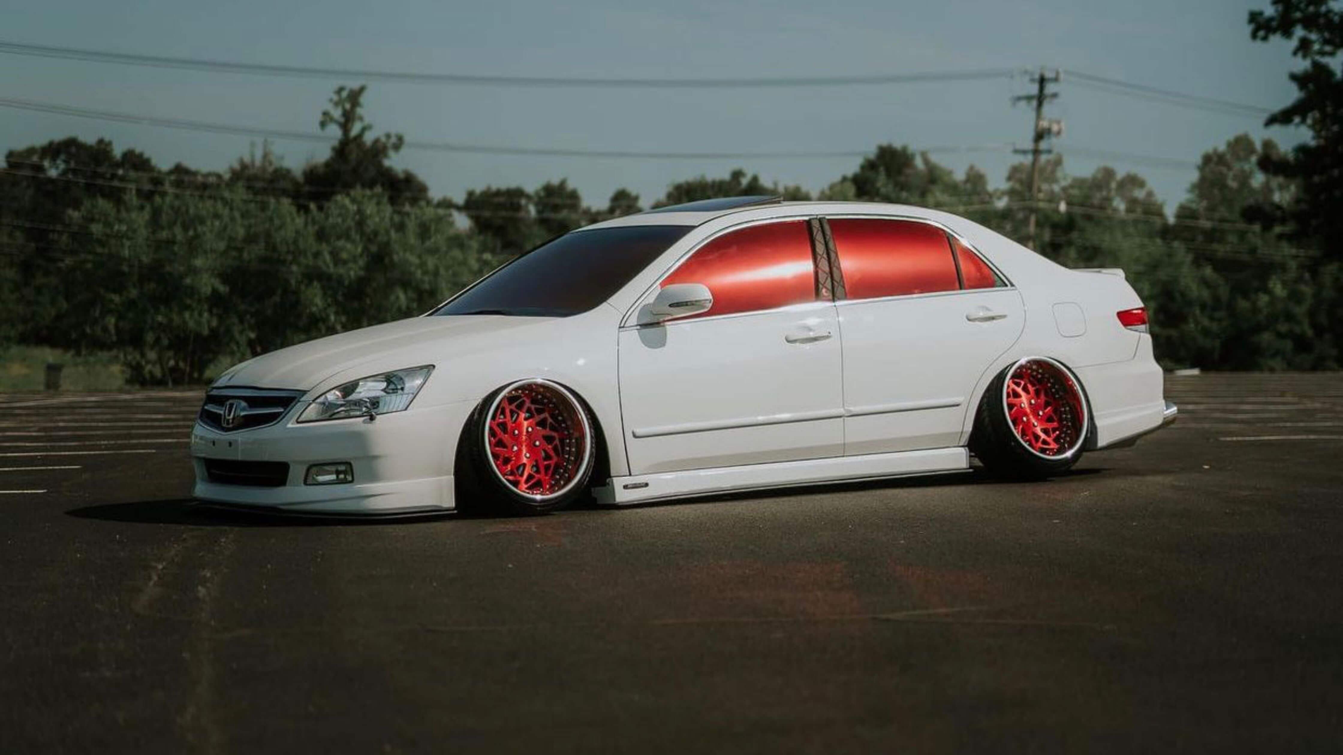 White car with red-tinted windows in an empty lot, showcasing tint style.