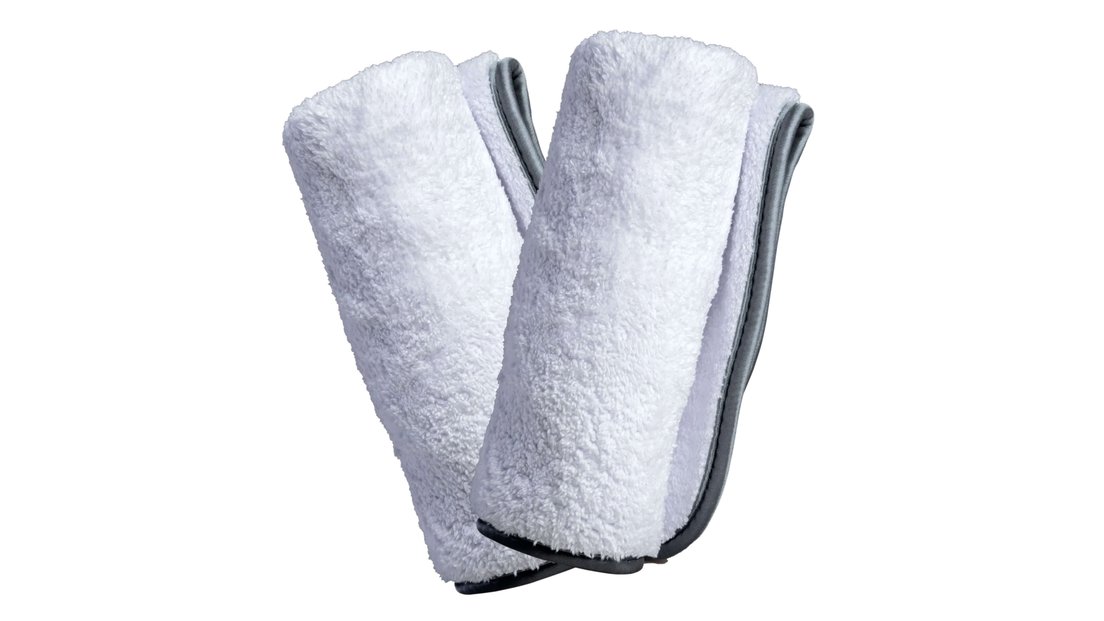 Two folded white microfiber towels with gray edges on a surface, representing proper drying techniques for microfiber cloths.