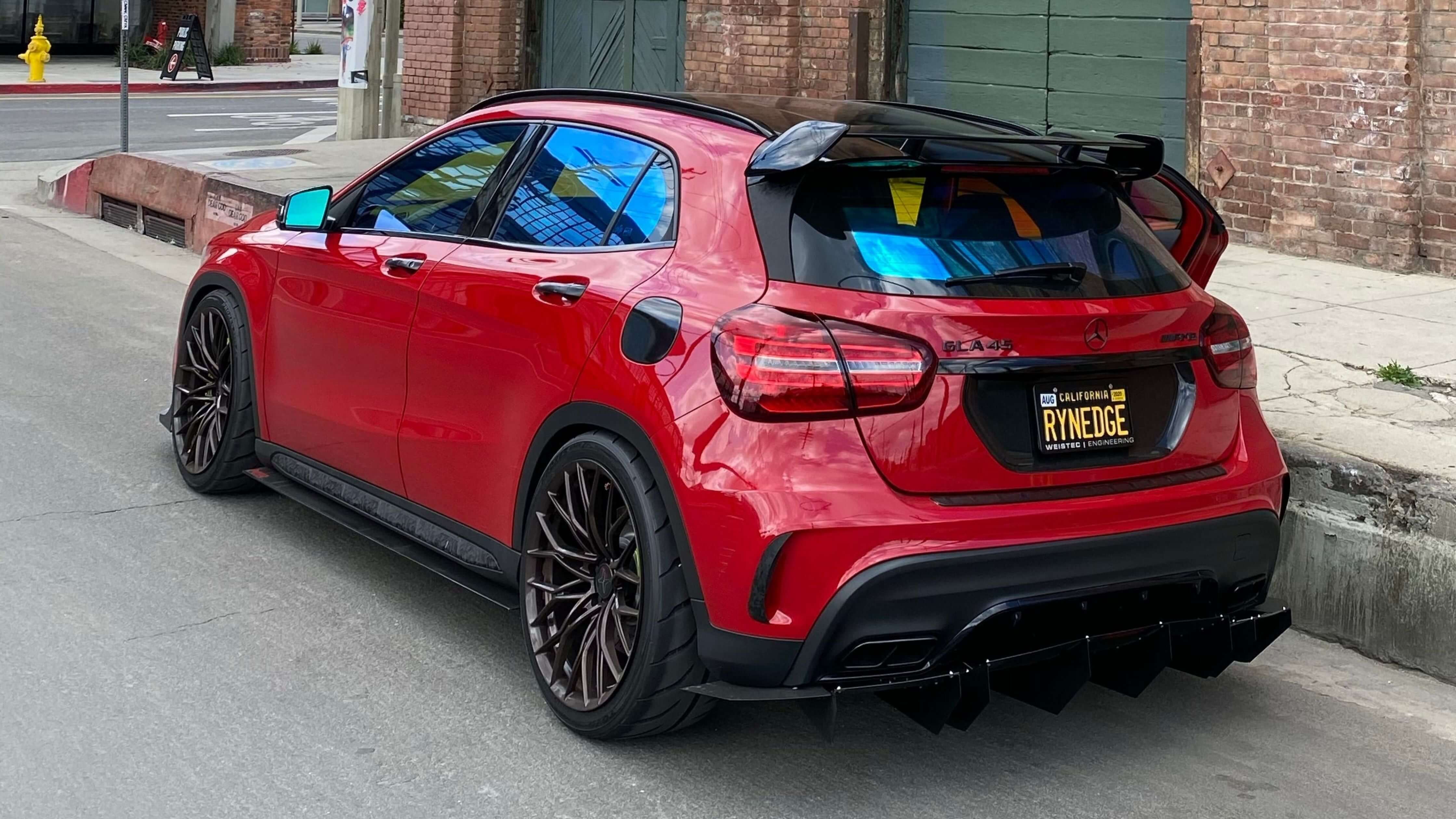 A red Mercedes-Benz GLA 45 AMG with tinted windows, custom wheels, and a spoiler, parked on a street.