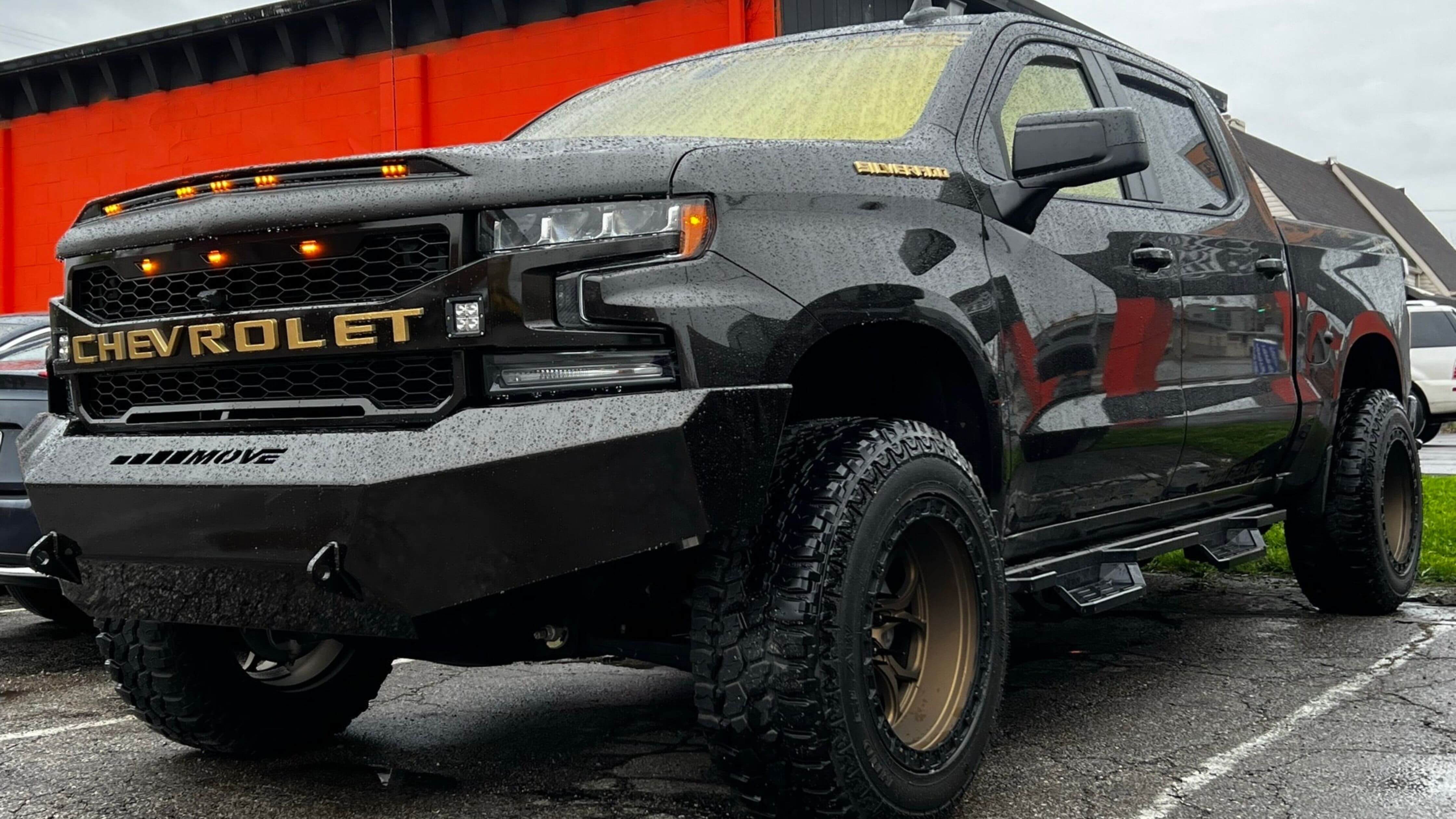 A black Chevrolet pickup truck with window tint parked in front of a red building.