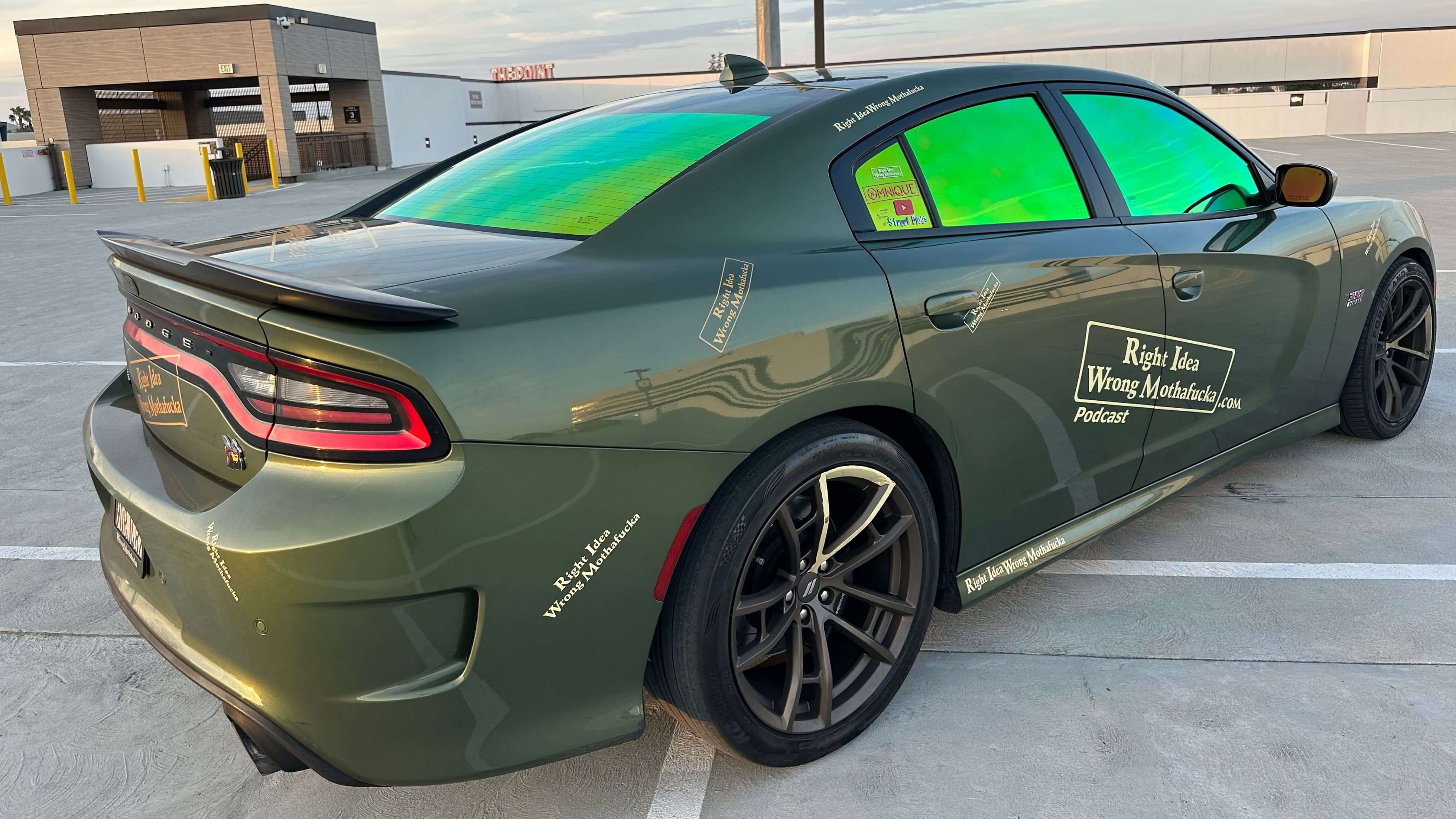 A green Dodge Charger with tinted windows and decals on a rooftop parking lot.