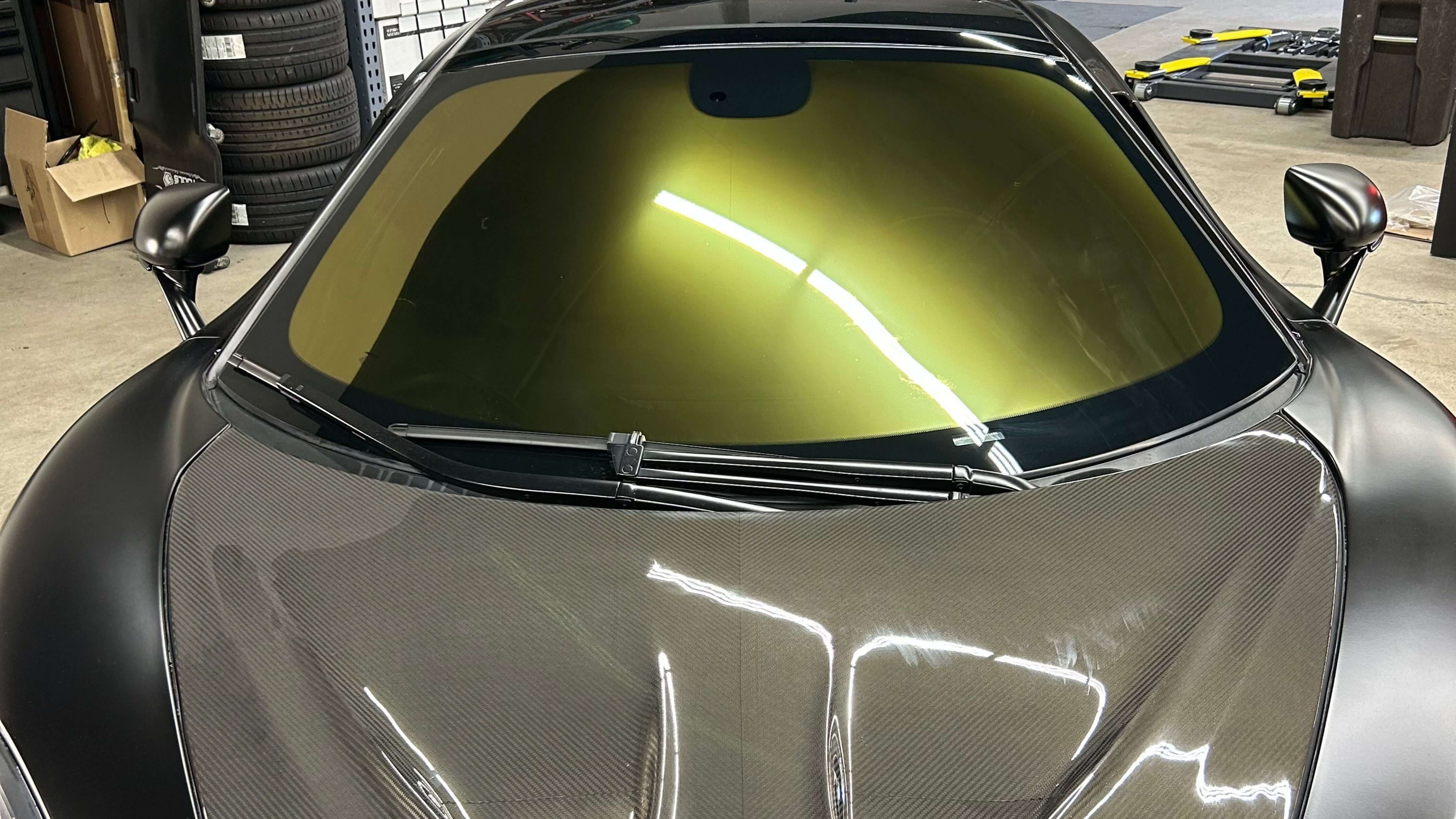 A close-up of a car with a carbon fiber hood and a yellow-tinted windshield in a garage.