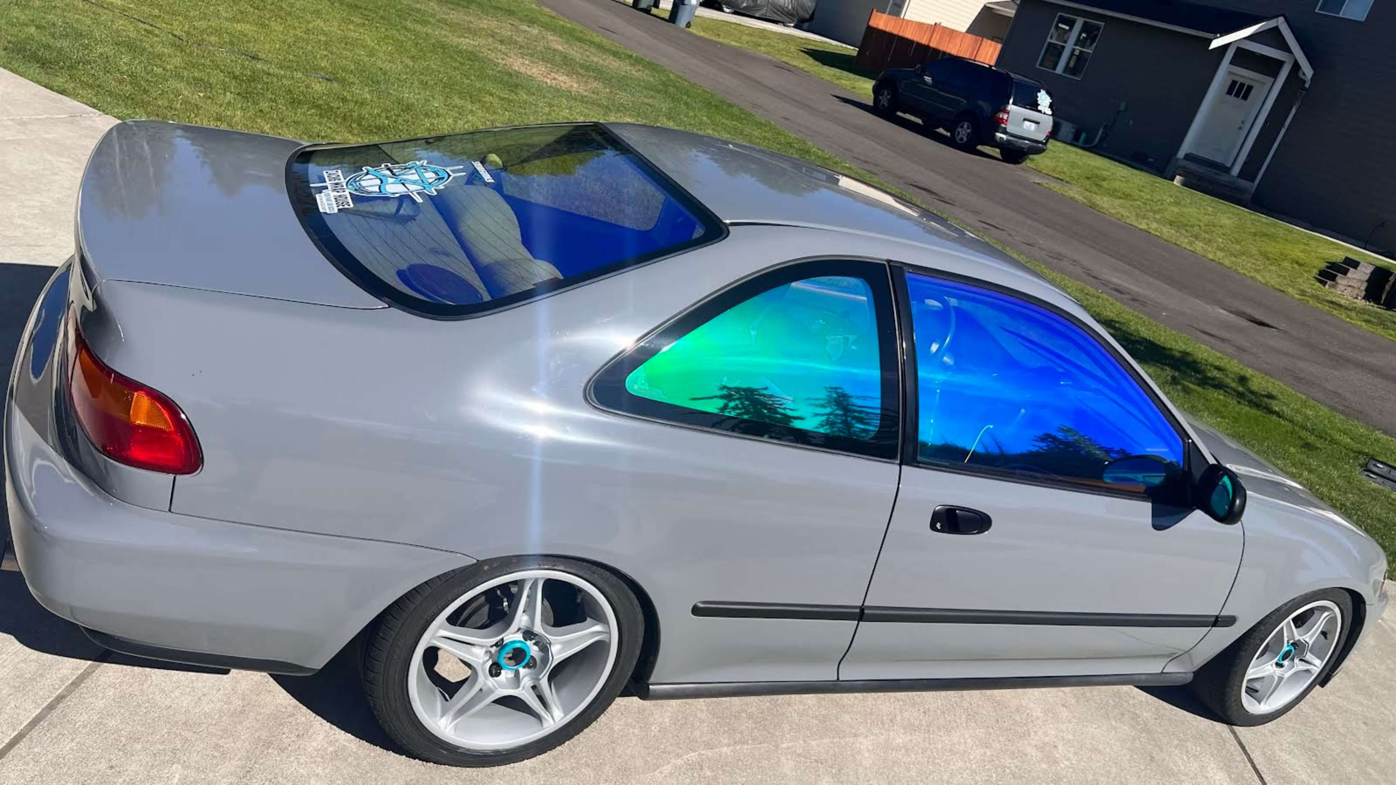 A gray coupe car with blue-tinted windows parked on a driveway, showcasing DIY window tinting.