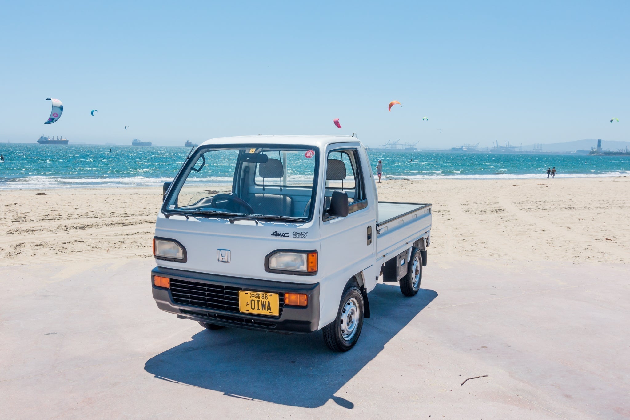 White Honda Acty mini truck parked at a sunny beach, highlighting its compact size, clean design, and versatility for outdoor and recreational use.
