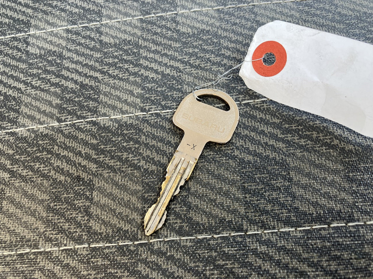 A metal key with a tag attached, placed on a textured fabric surface.