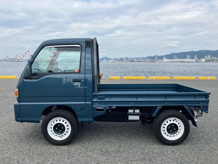 Subaru Sambar kei truck showcasing lightweight design by a waterfront.
