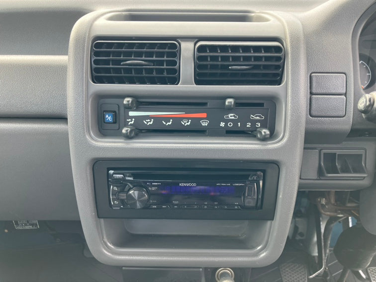 Close-up of Subaru Sambar dashboard showcasing air conditioning controls and Kenwood stereo, highlighting classic design and functionality.