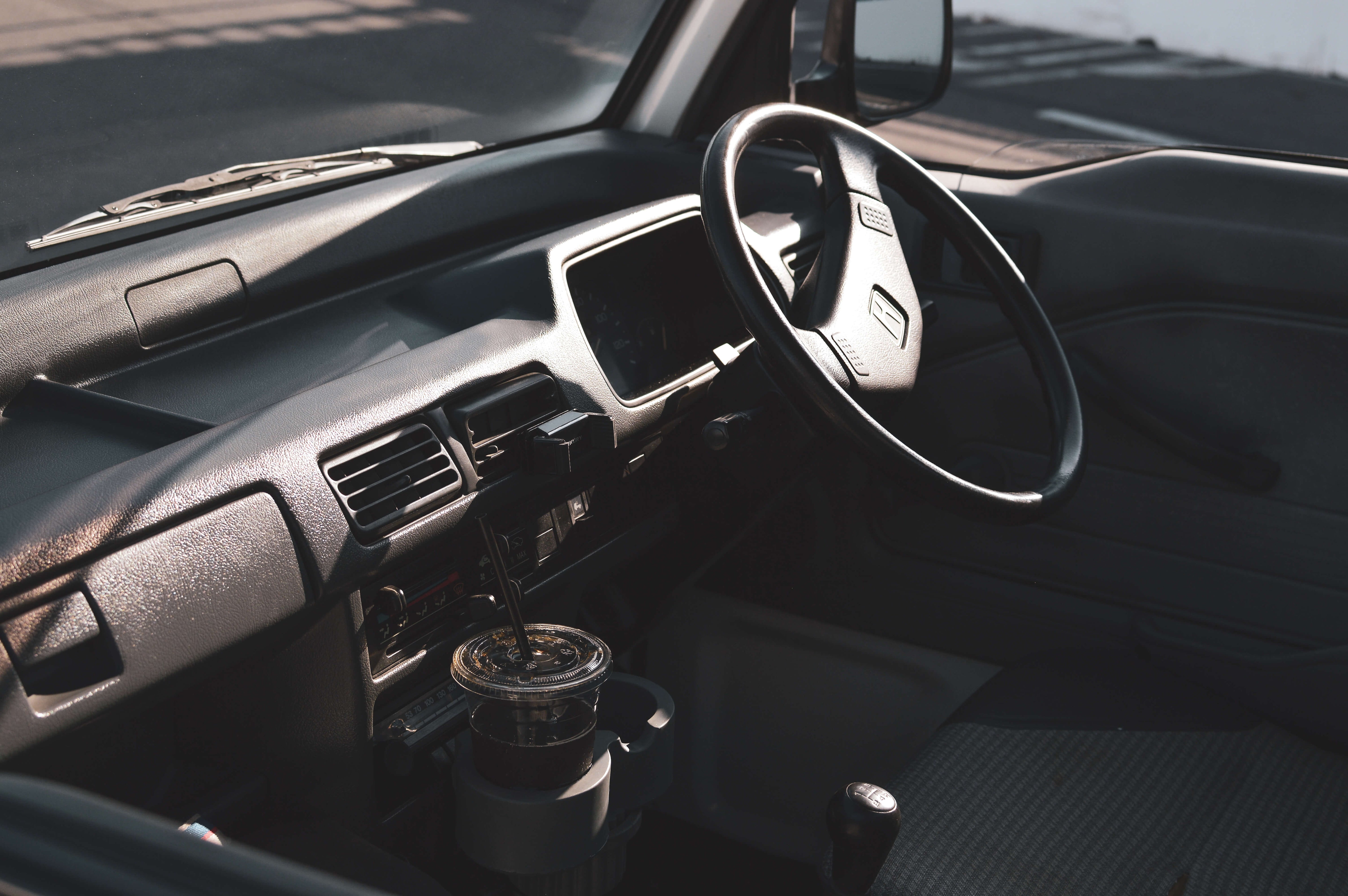 Interior of a kei truck in Minnesota, featuring a simple dark gray dashboard, black steering wheel, and sunlight casting shadows, highlighting Japanese design.