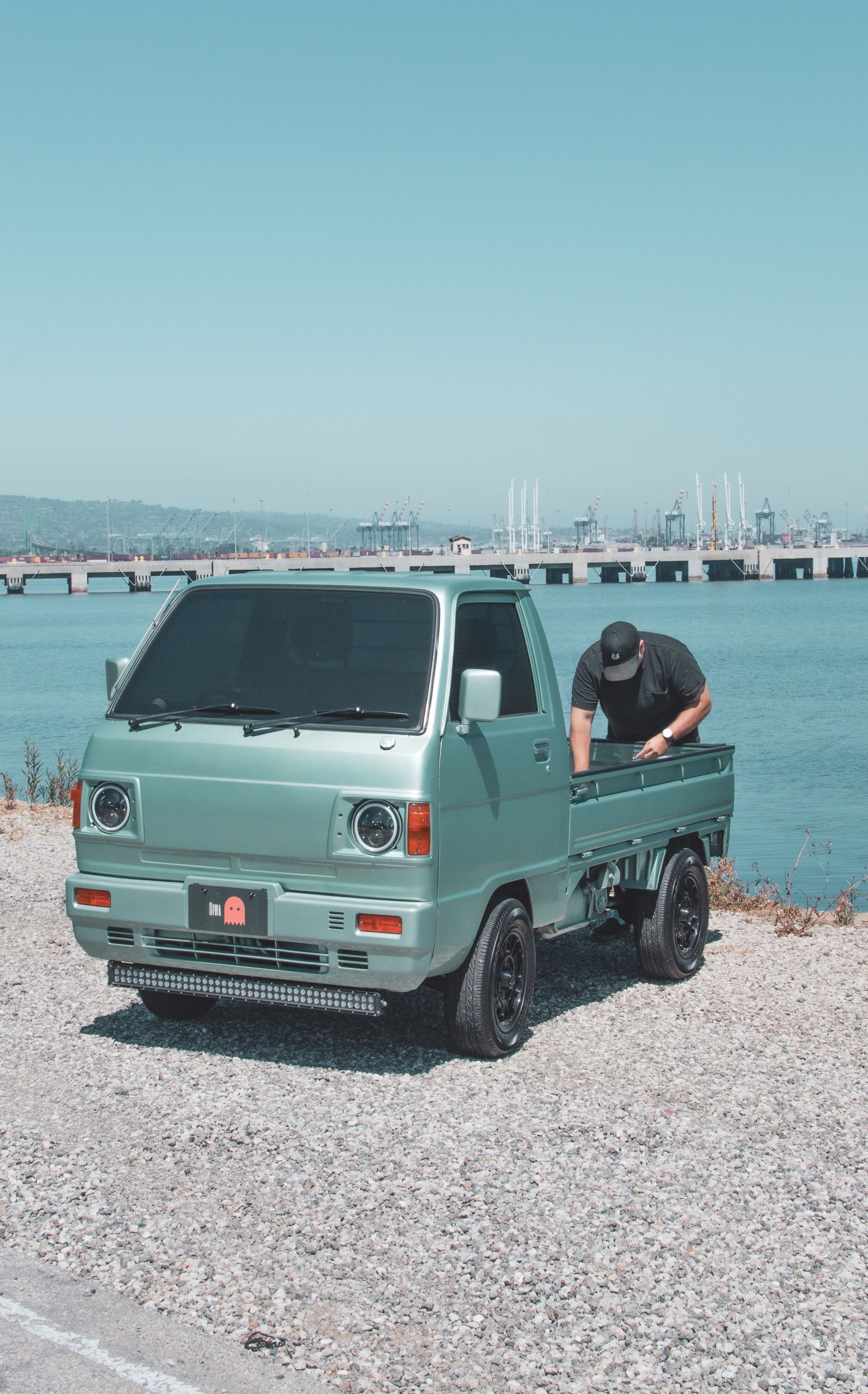 White Suzuki Carry mini truck parked on a city street, showcasing compact design and efficient cargo transport capabilities.