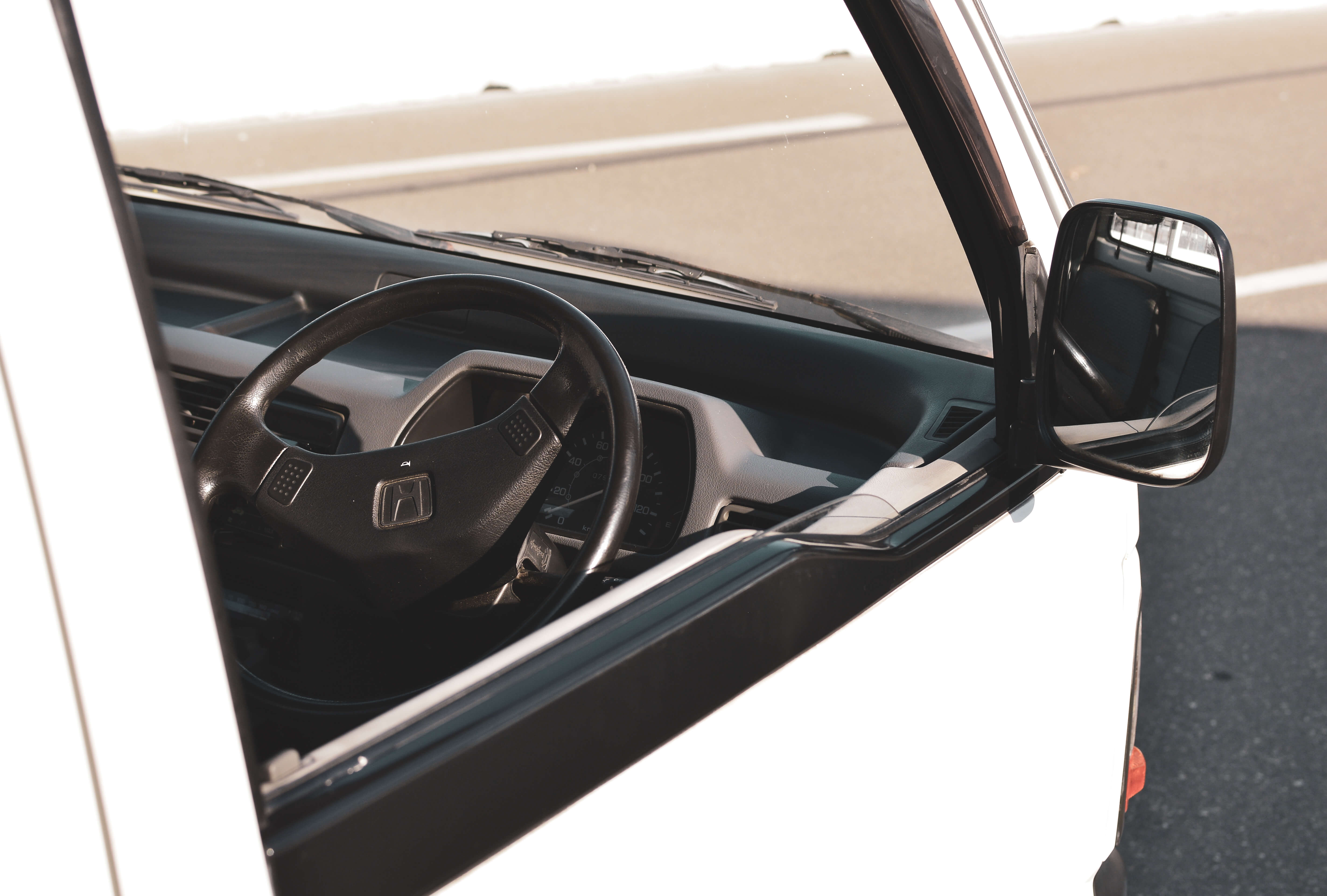 Interior of a white RC kei truck showcasing the steering wheel, dashboard, and side mirror reflecting the road.