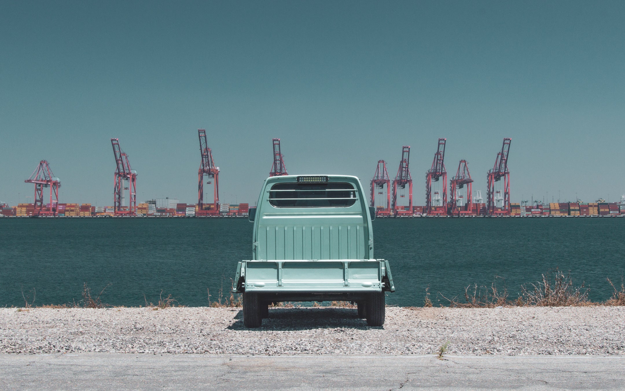 A kei truck parked by Michigan waterside with cranes and containers in view.