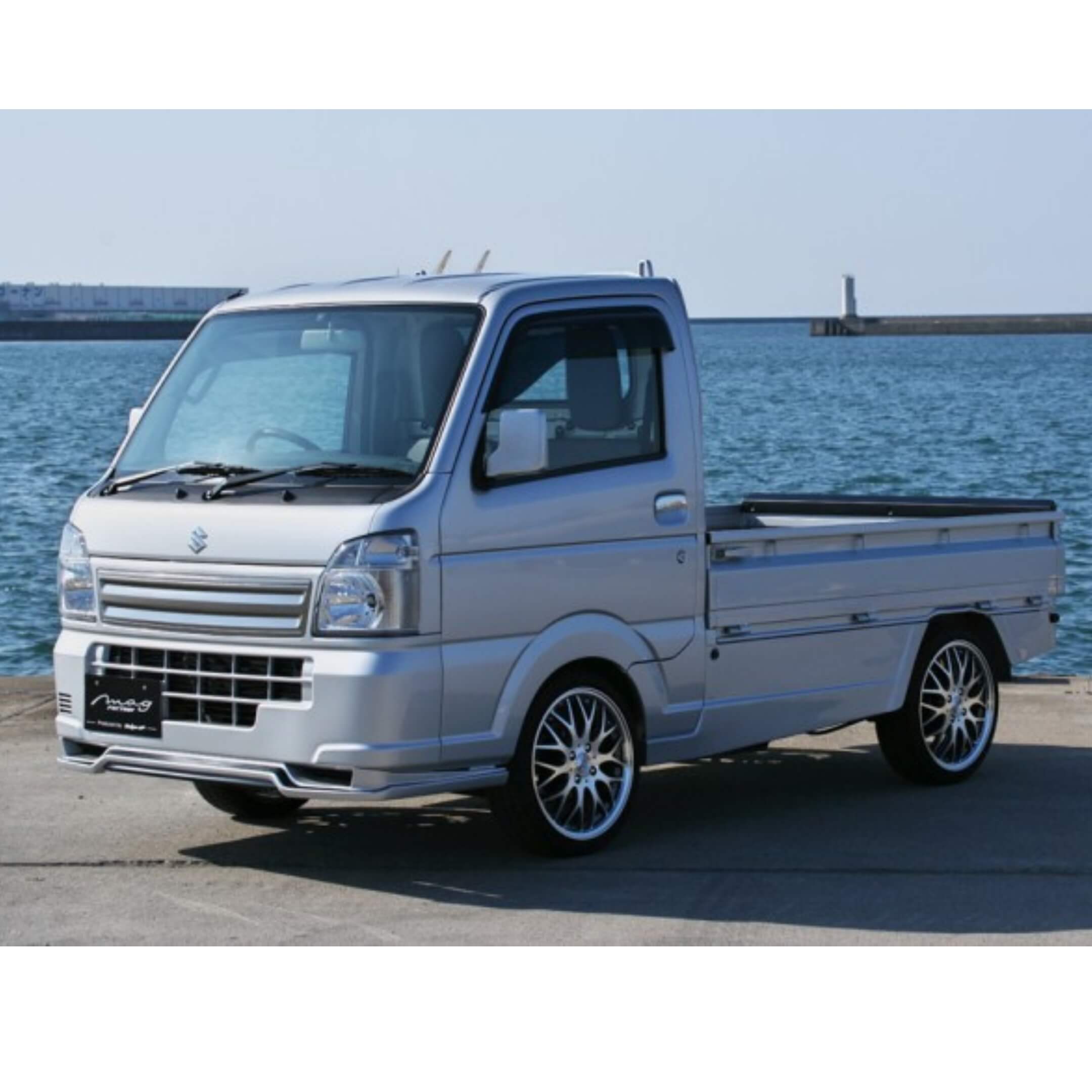 Silver Suzuki Carry DA16T with front spoiler body kit, 2013-2023 model, parked by the sea.