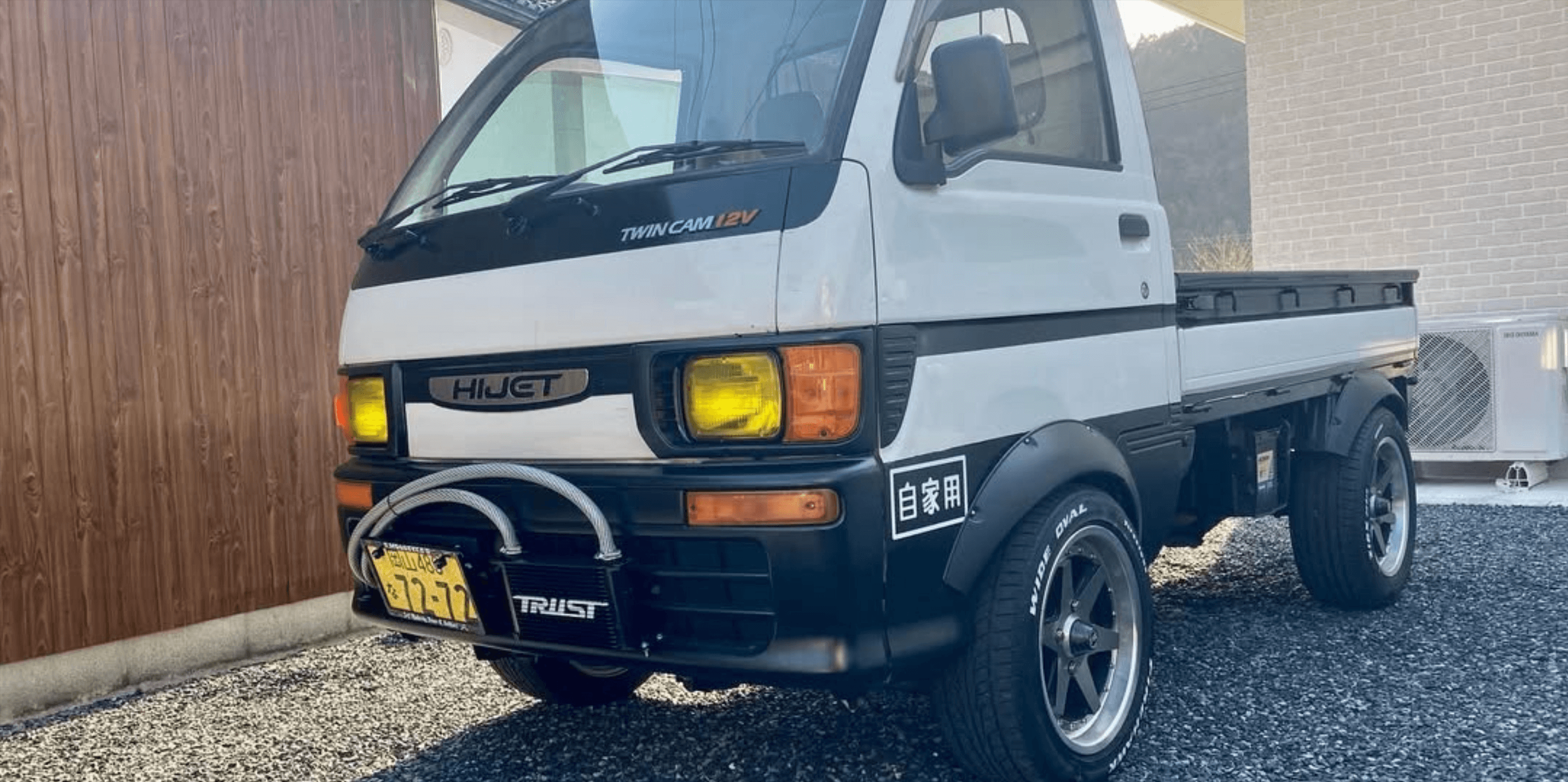 1997 Daihatsu Hijet S100P Twin Cam 12V kei truck in white featuring aftermarket Trust front-mounted oil cooler with braided stainless hoses, yellow-tinted headlights, black flared fender arches, and five-spoke deep-dish alloy wheels.
