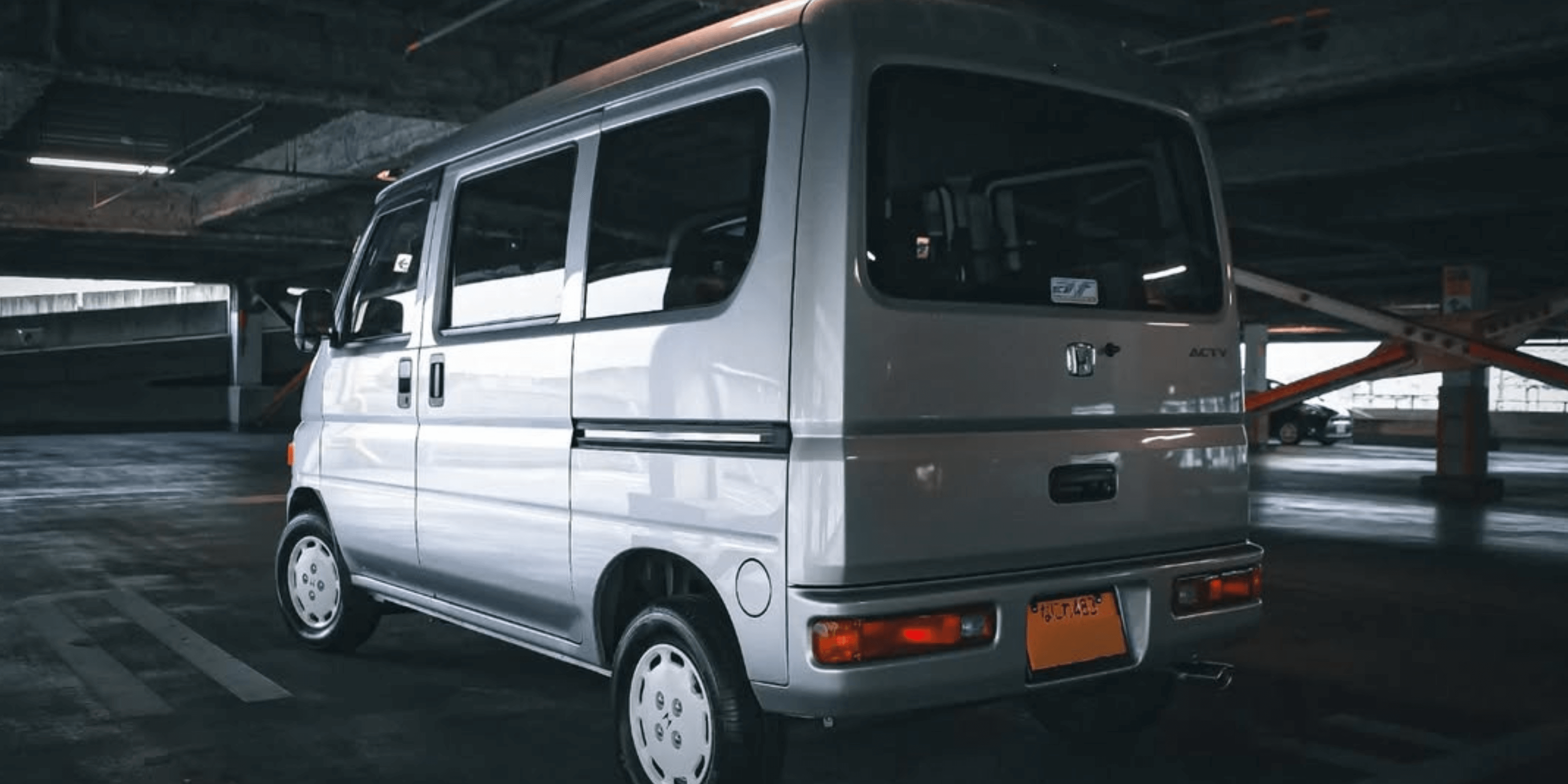 2004 Honda Acty Van HH6 silver kei microvan rear three quarter view parked in dim underground parking garage showcasing compact Japanese city van styling