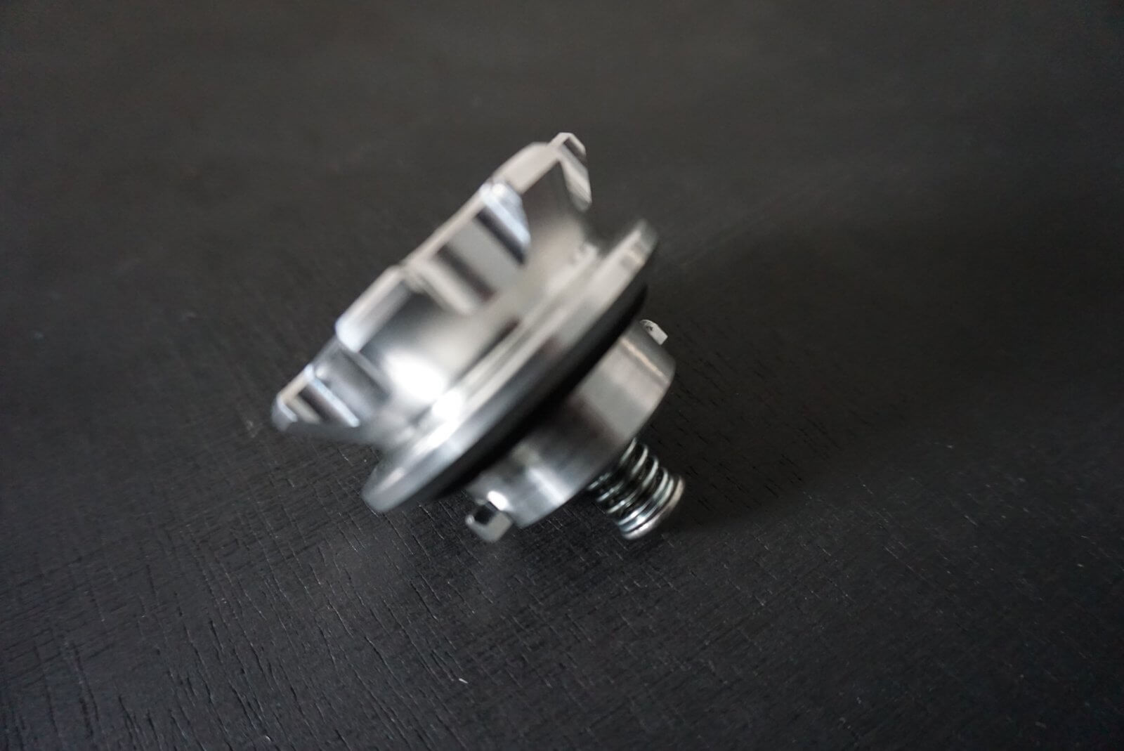 Crown gas cap for Honda Acty Van, silver metal with a spring mechanism, angled view on a dark background