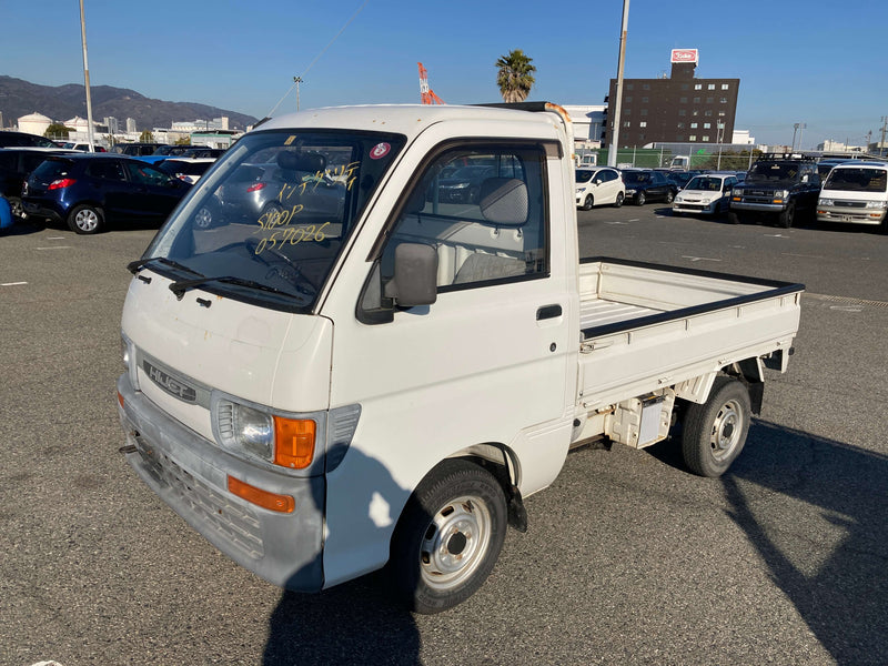White 1998 Daihatsu Hijet S100P Kei Truck parked outdoors, featuring rectangular headlights, clean body lines, and a spacious cargo bed, perfect for versatile use, showcased on Oiwa Garage’s informative Kei truck page.