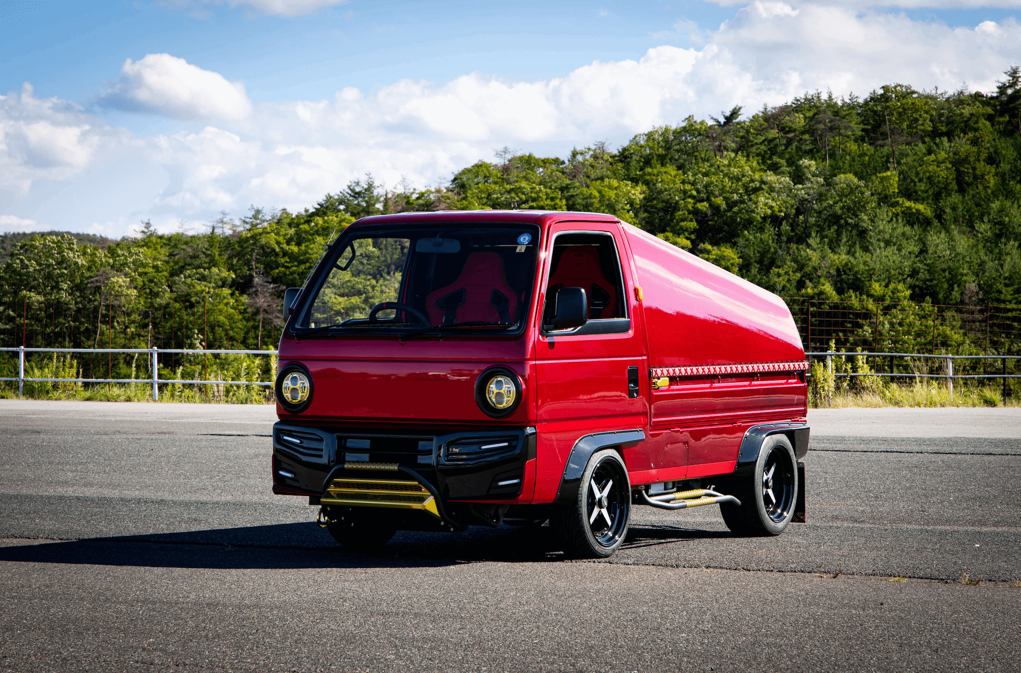 1989 Honda Acty kei truck in vibrant red with custom aerodynamic canopy body kit, lowered suspension, black multi-spoke alloy wheels, gold front skid plate, and racing bucket seat
