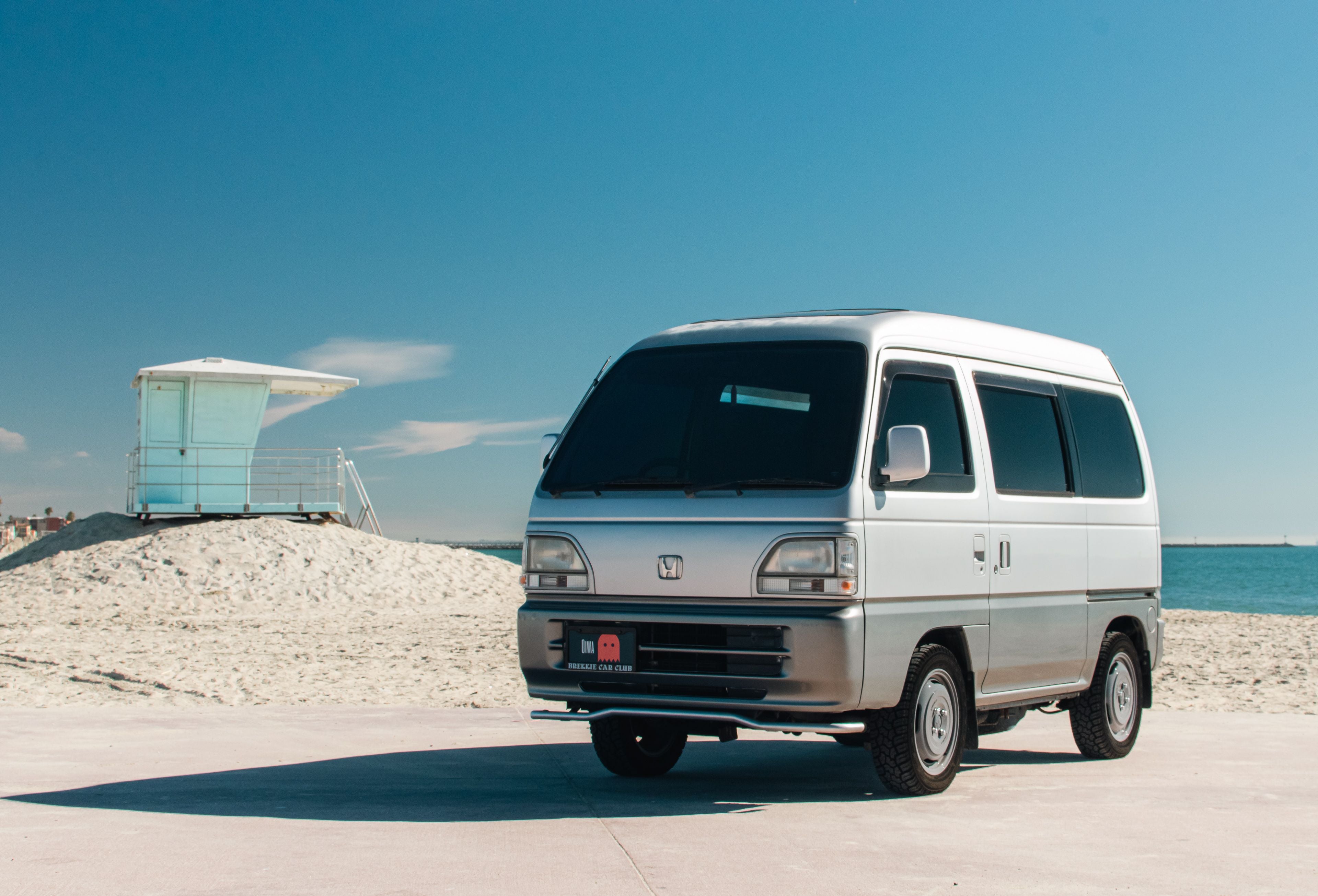 Sleek silver 1998 Honda Acty Van (HH3, HH4) parked at a sunny beach, highlighting premium Honda Acty parts and accessories from Oiwa Garage.