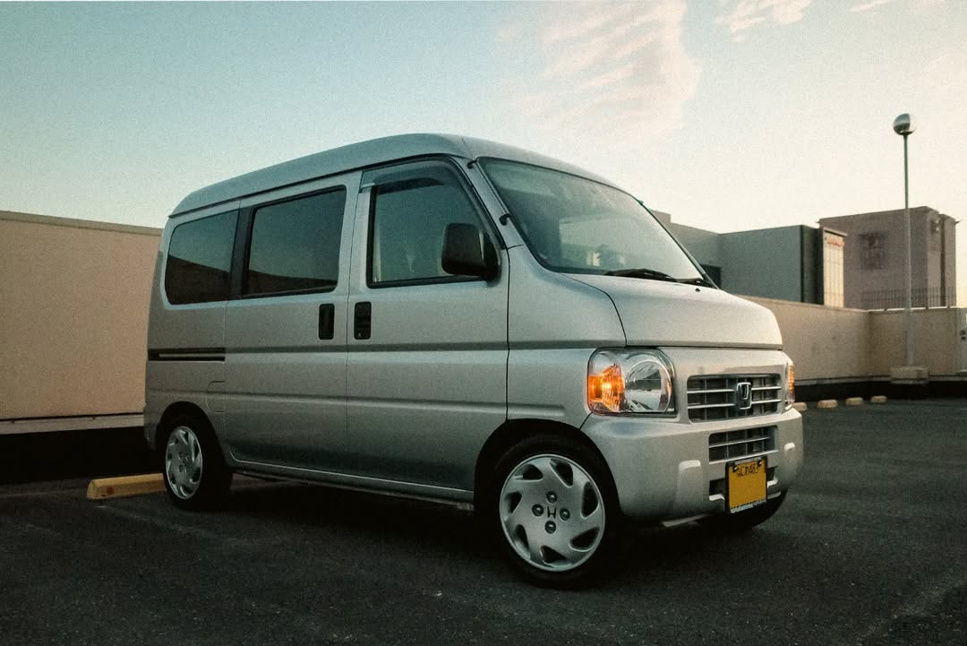 Silver 2002 Honda Acty Van HH6 parked in urban setting at sunset, showcasing authentic Honda Acty parts and accessories from Oiwa Garage.