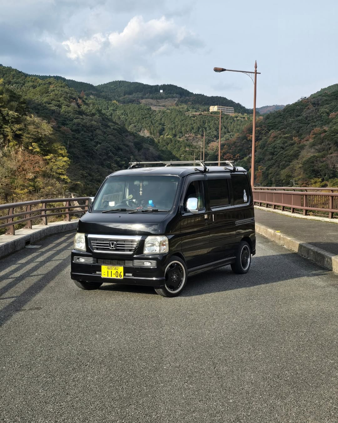 Black 2007 Honda Vamos HM2 Van parked on a scenic mountain road, highlighting premium Honda Acty and Vamos parts and accessories from Oiwa Garage.