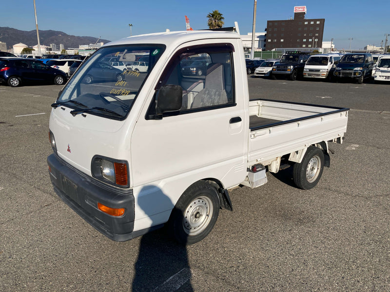 White 1995 Mitsubishi Minicab U42T Kei Truck parked in an open lot, featuring distinctive rectangular headlights, compact design, and practical cargo bed, showcased prominently on Oiwa Garage’s comprehensive Kei truck information webpage.