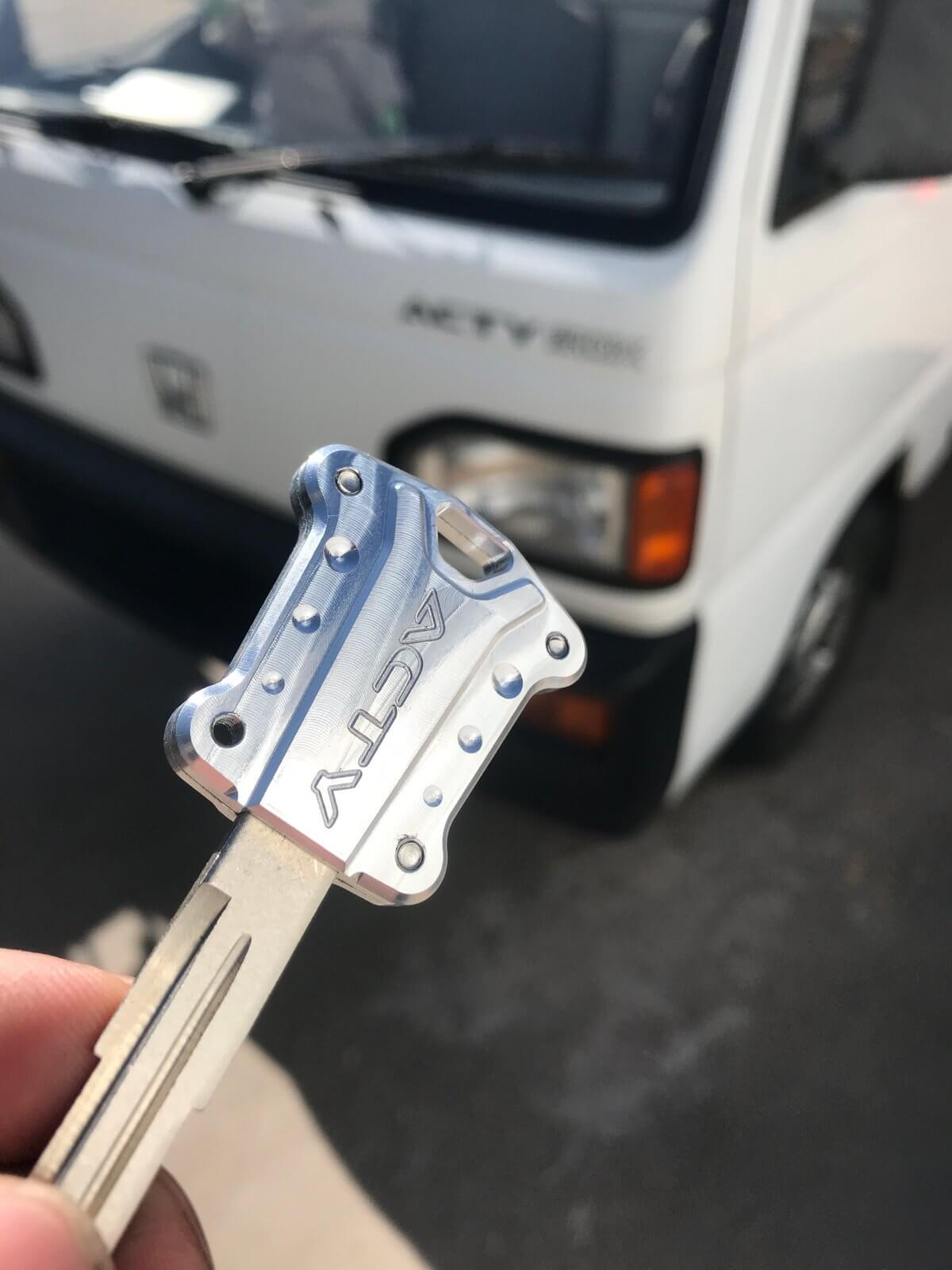 CNC-machined 6061 aluminum key cover for Honda Acty Vans, enhancing style with a durable upgrade, shown with a vehicle in the background.