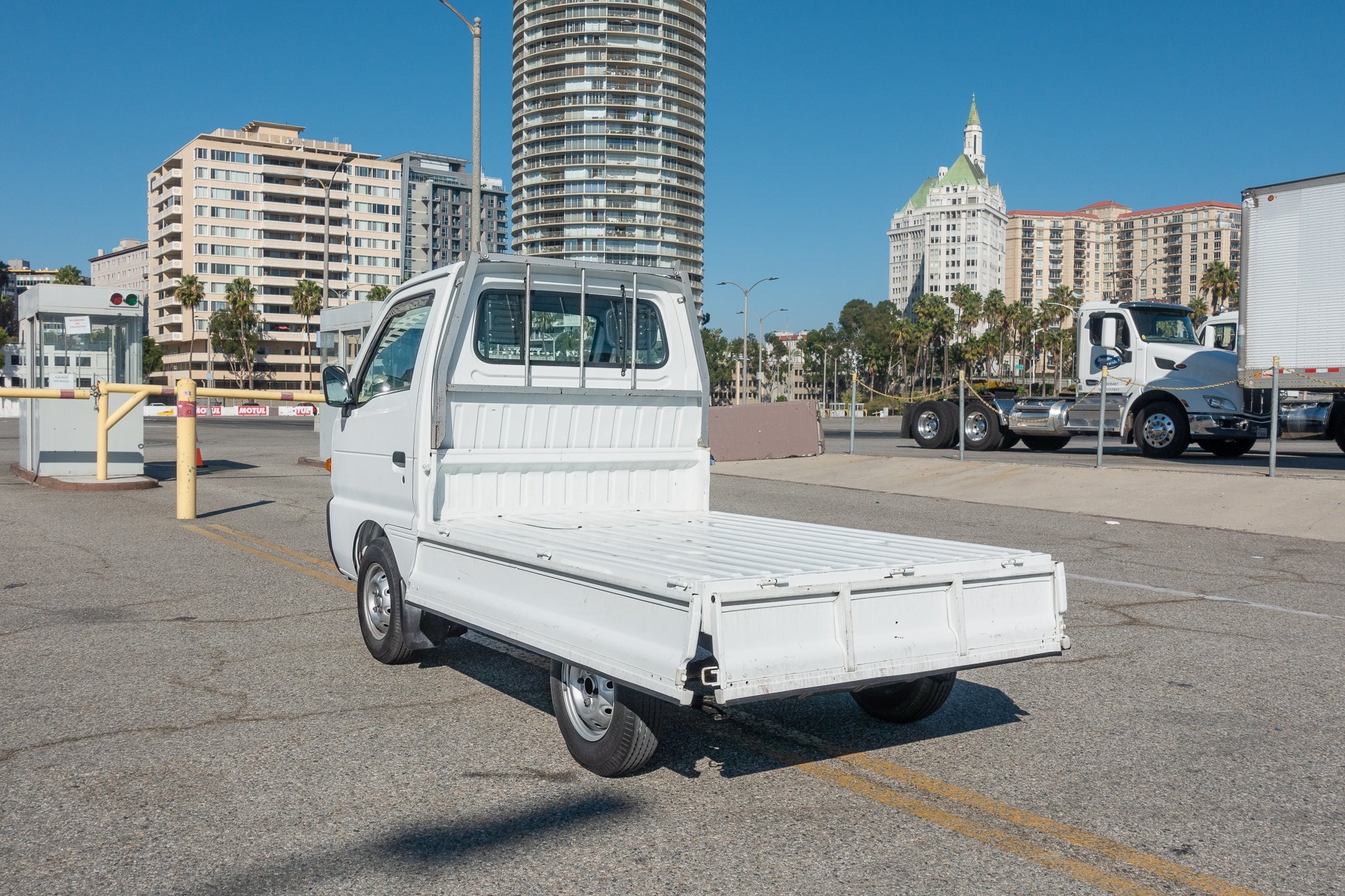 A small white flatbed truck is parked in an urban area with tall buildings in the background.