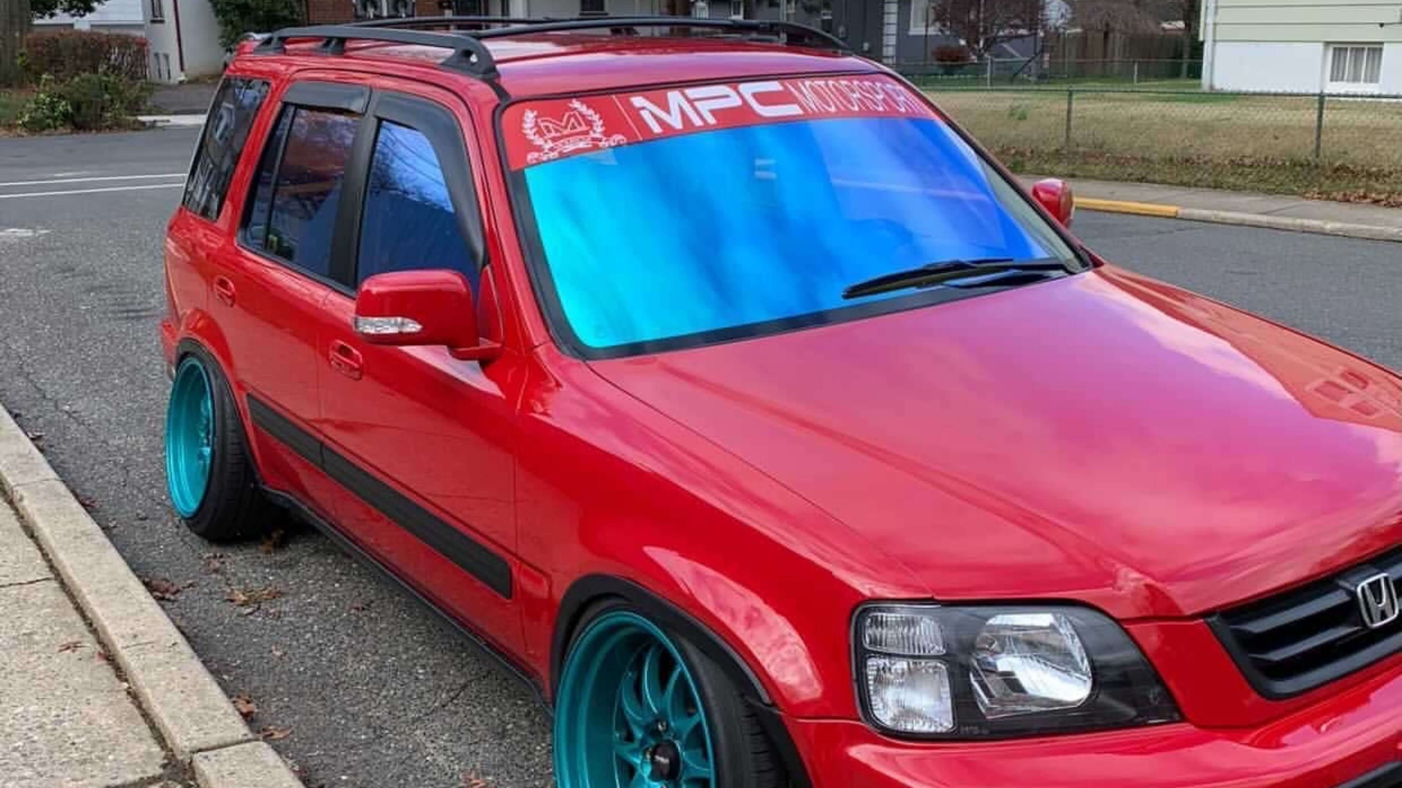 Red Honda SUV with blue-tinted windows and teal wheels parked on the street.