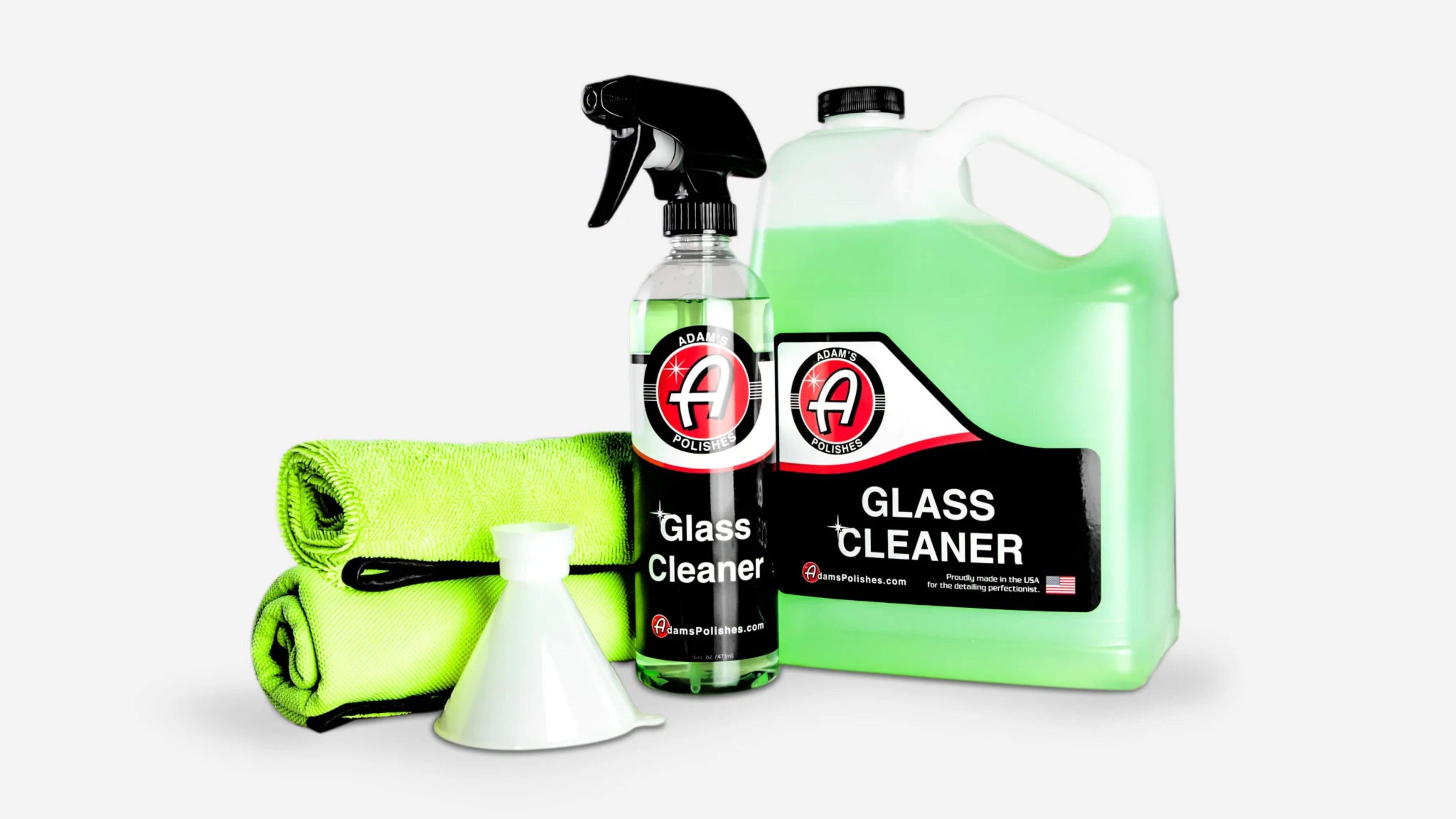 A set of glass cleaning products including a spray bottle, a large refill container, two green microfiber cloths, and a white funnel, ideal for achieving streak-free car windows.