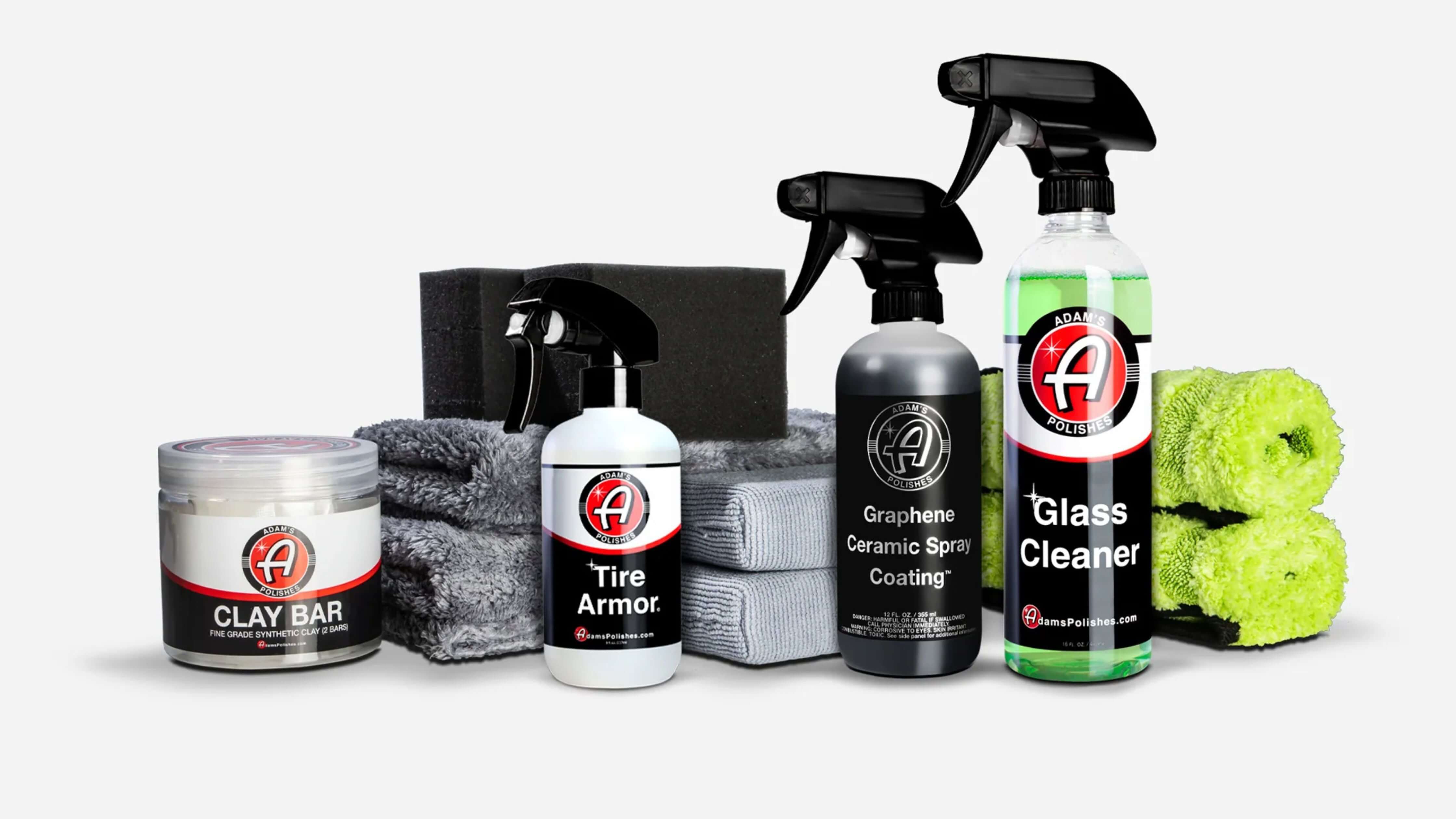 A collection of car care products including clay bar, tire armor, graphene ceramic spray coating, and glass cleaner, accompanied by microfiber towels and sponges.