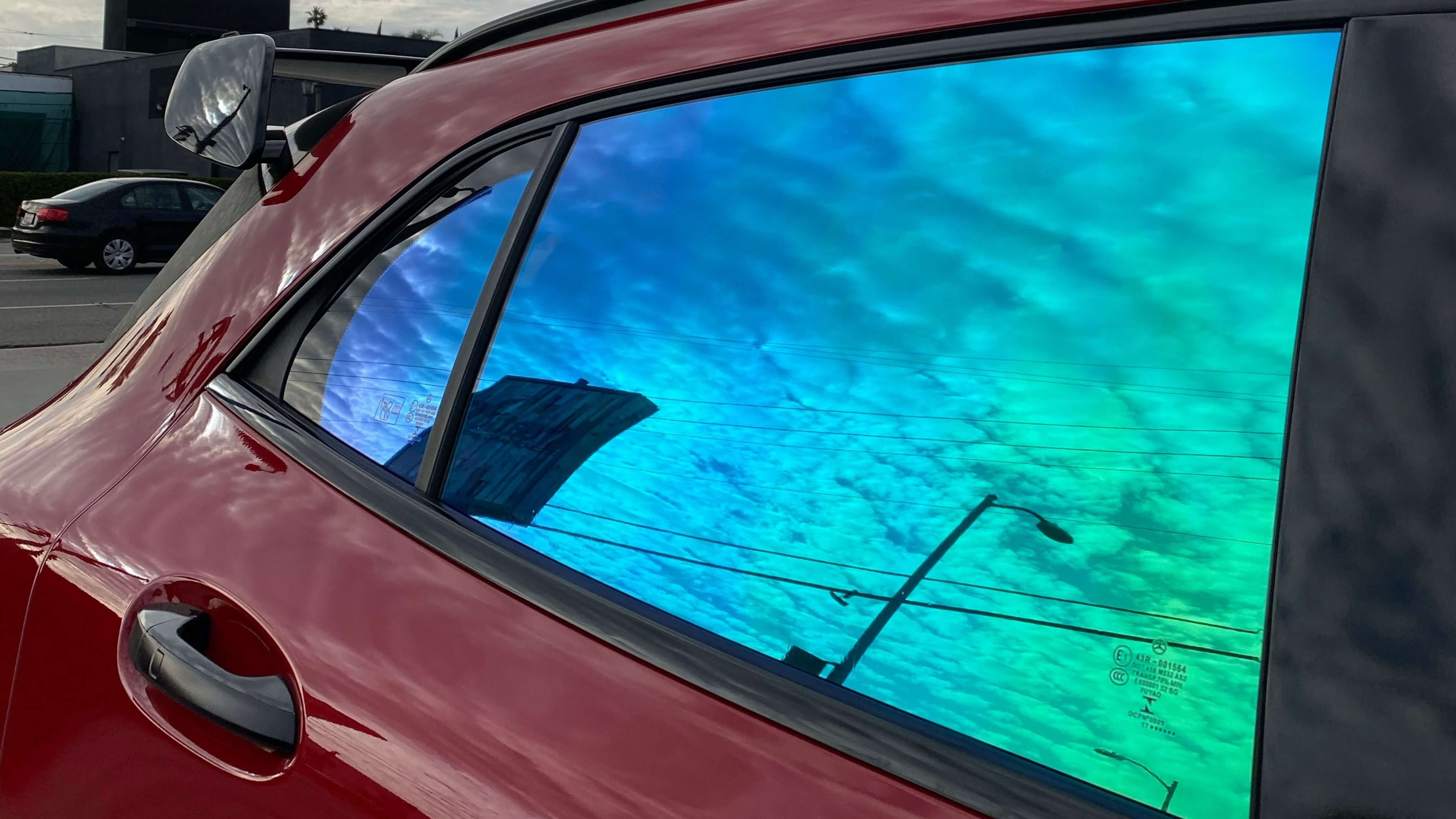 Removing old tint from a red car window reflecting a vibrant sky.